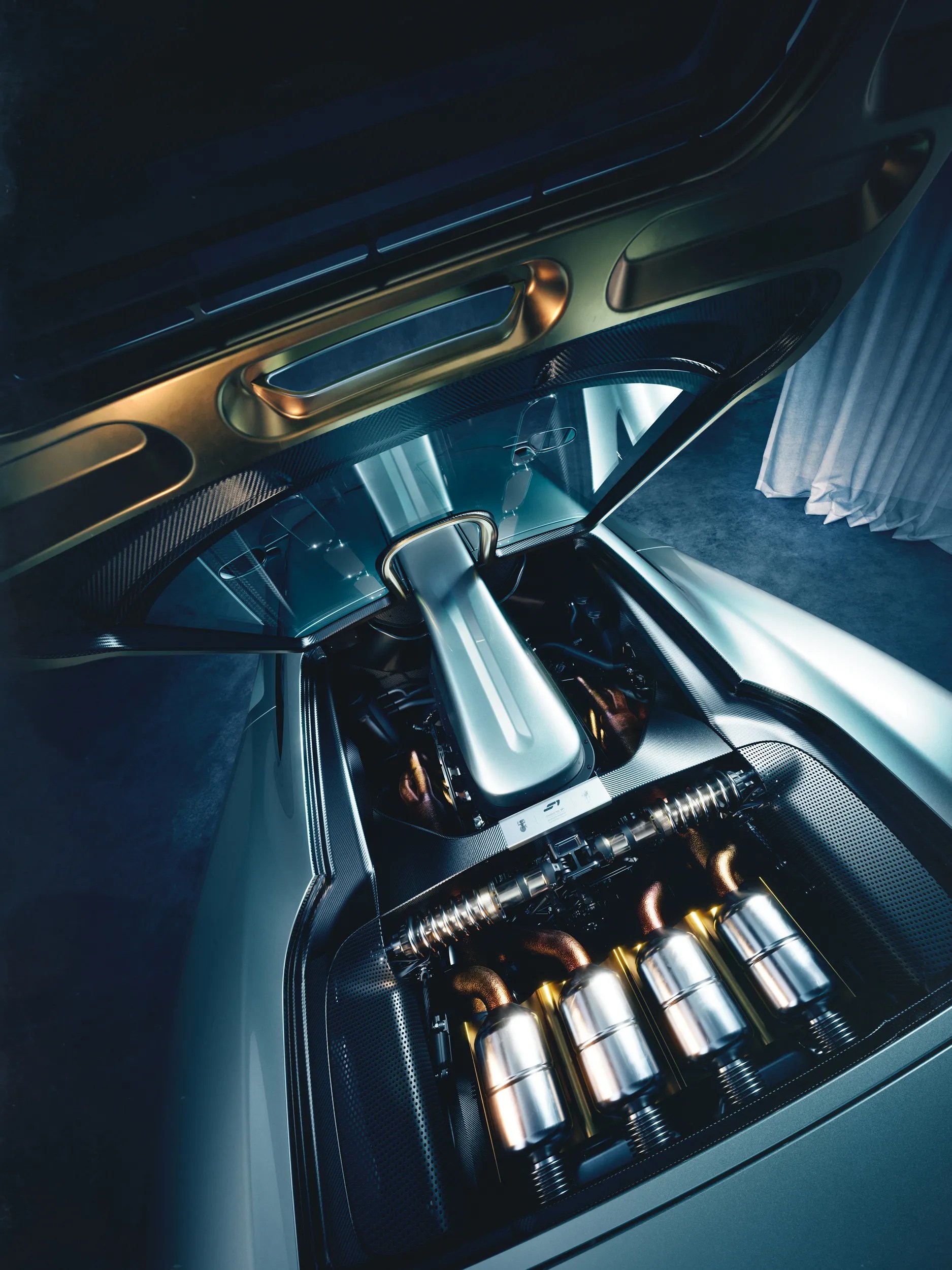 Vista superior do motor de um carro esportivo, com detalhes em dourado e prateado, e quatro saídas de escape metálicas visíveis