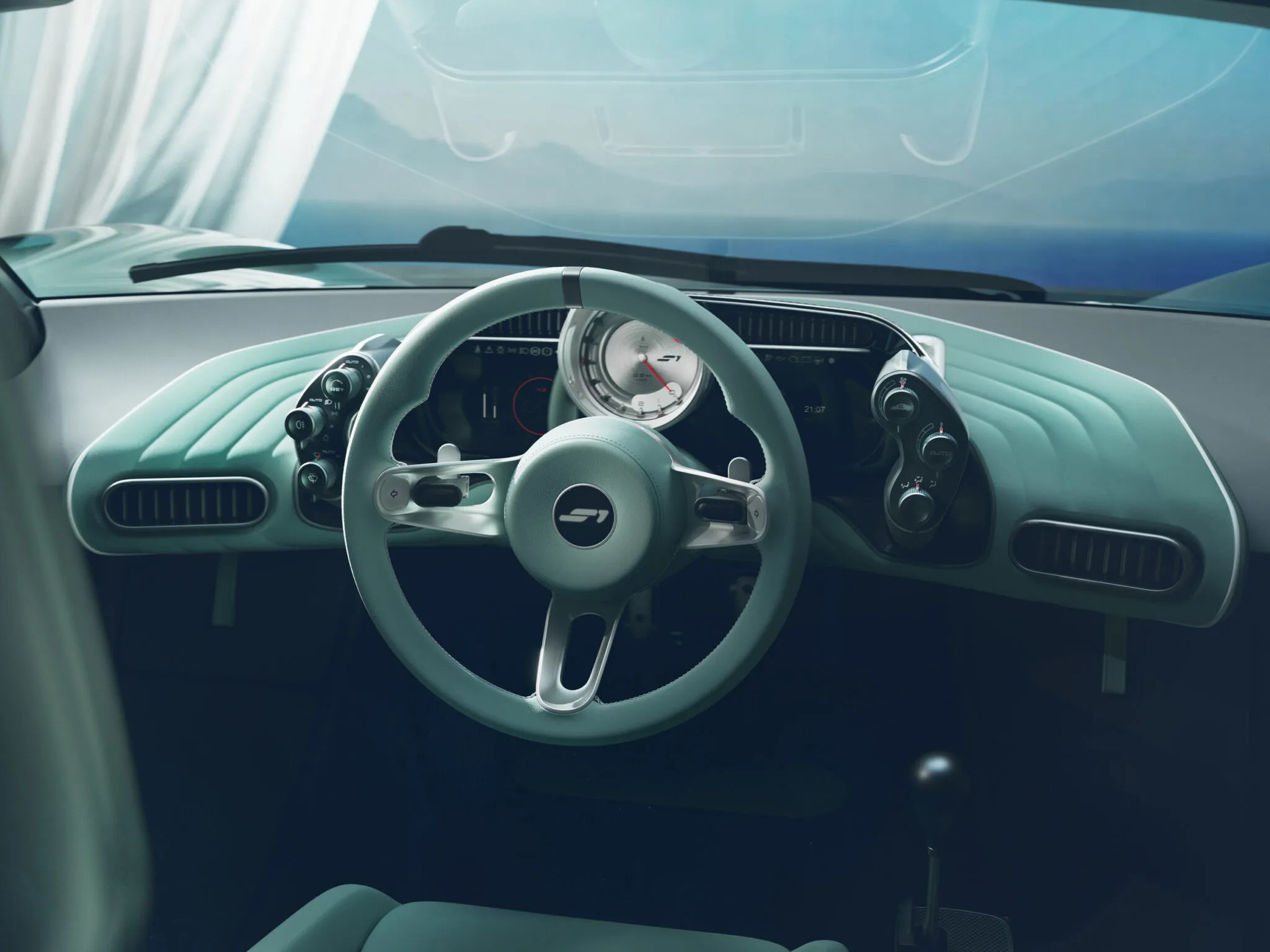 Interior de um carro com painel e volante em tom verde-água. O volante tem um logotipo S1 no centro e detalhes prateados. O painel possui um velocímetro analógico e telas digitais, além de saídas de ar e botões de controle. O para-brisa reflete o céu azul e uma paisagem distante