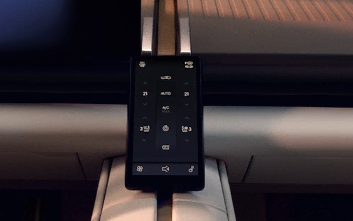 Tela de controle digital de um carro, exibindo configurações de ar-condicionado com temperatura 21 graus, modo automático e botões para ventilação e outras funções. Na parte inferior, ícones de aplicativos e música. A tela está encaixada em um suporte no painel do veículo, com detalhes em tons escuros e claros