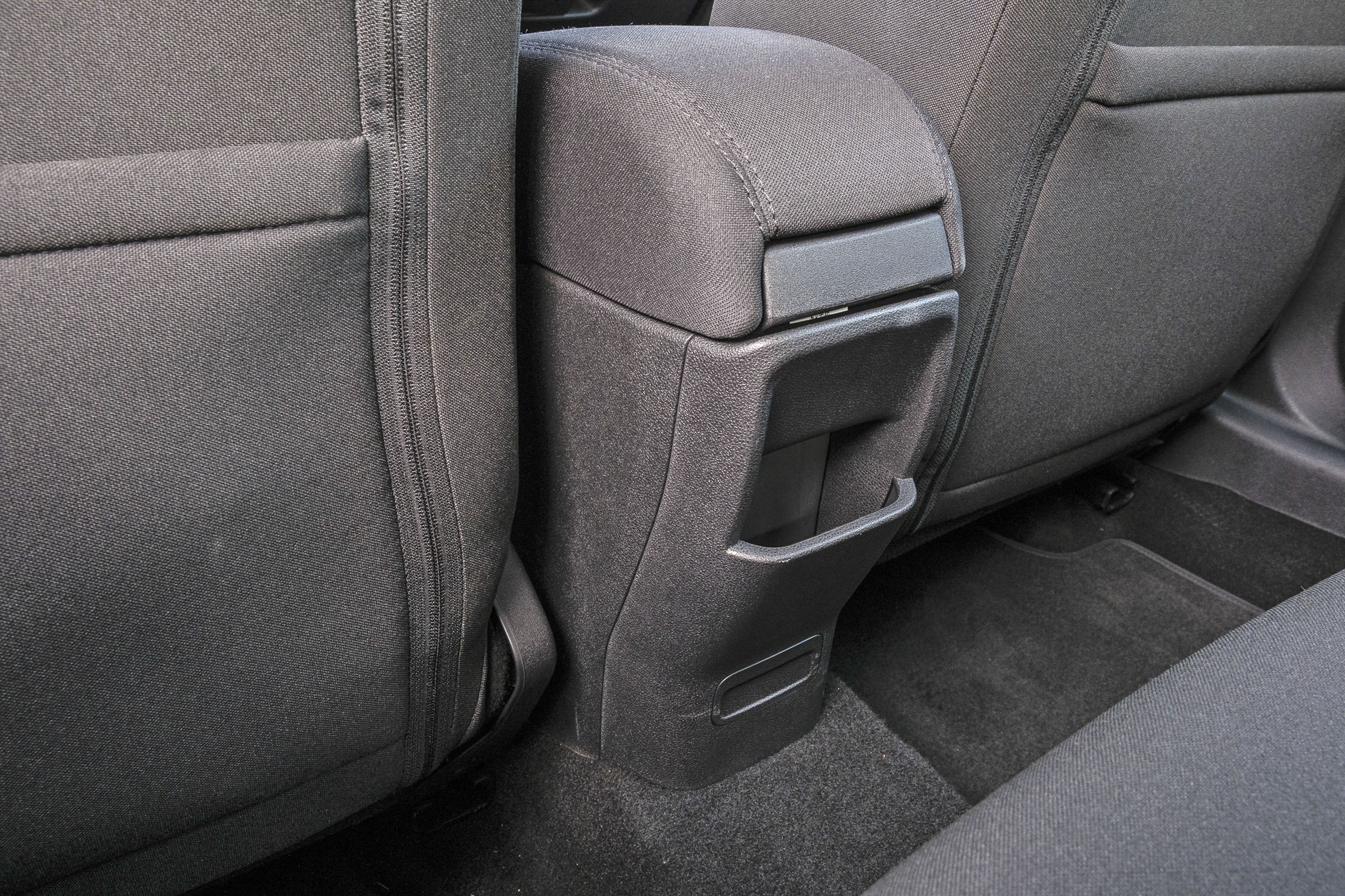 Console central de um carro, cinza escuro, com porta-objetos e apoio de braço estofado, entre dois bancos traseiros de tecido cinza
