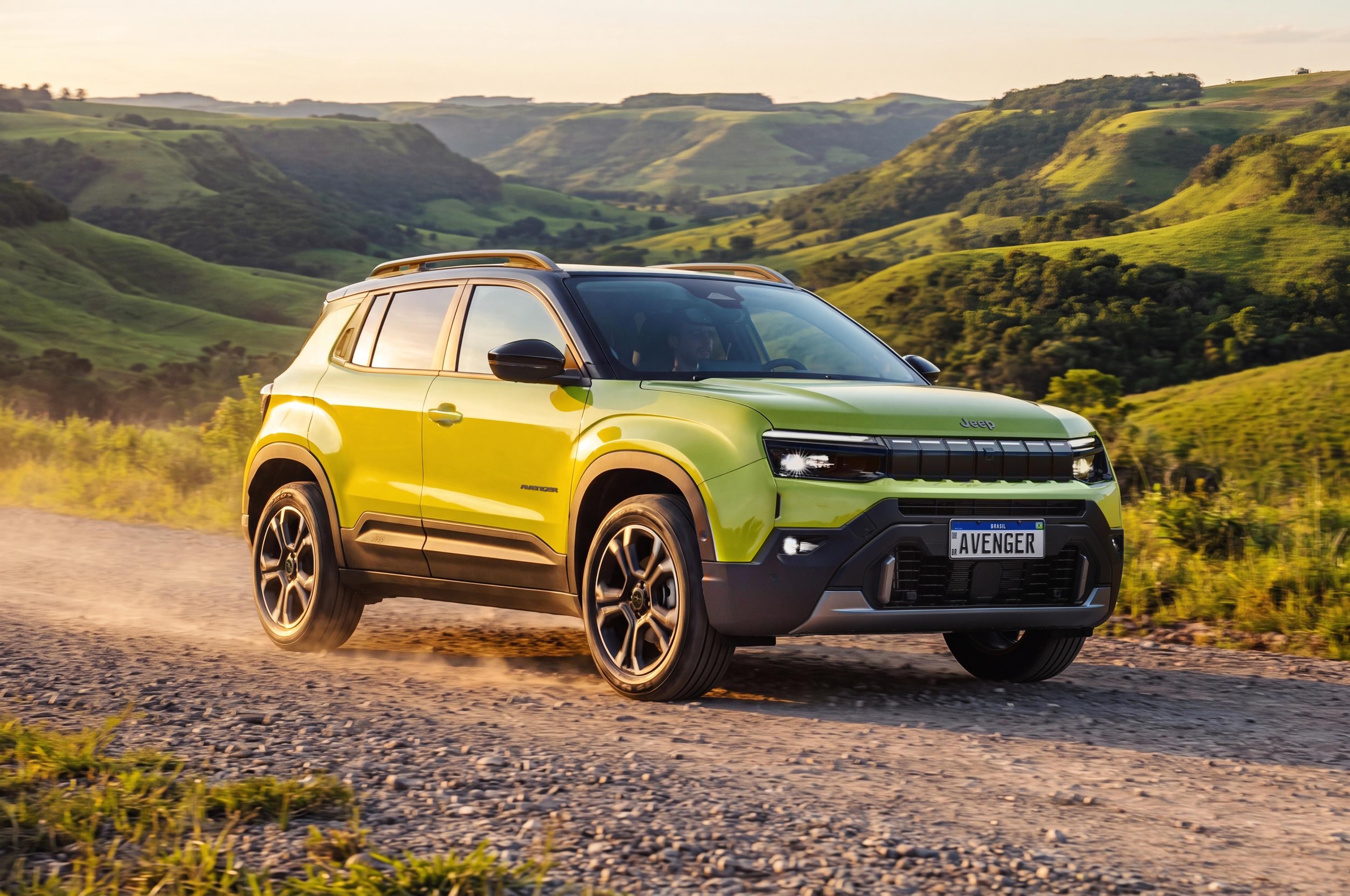 SUV Jeep Avenger amarelo-limão com teto preto e rack de teto, em estrada de terra com poeira, contra um cenário de colinas verdes e céu claro ao pôr do sol