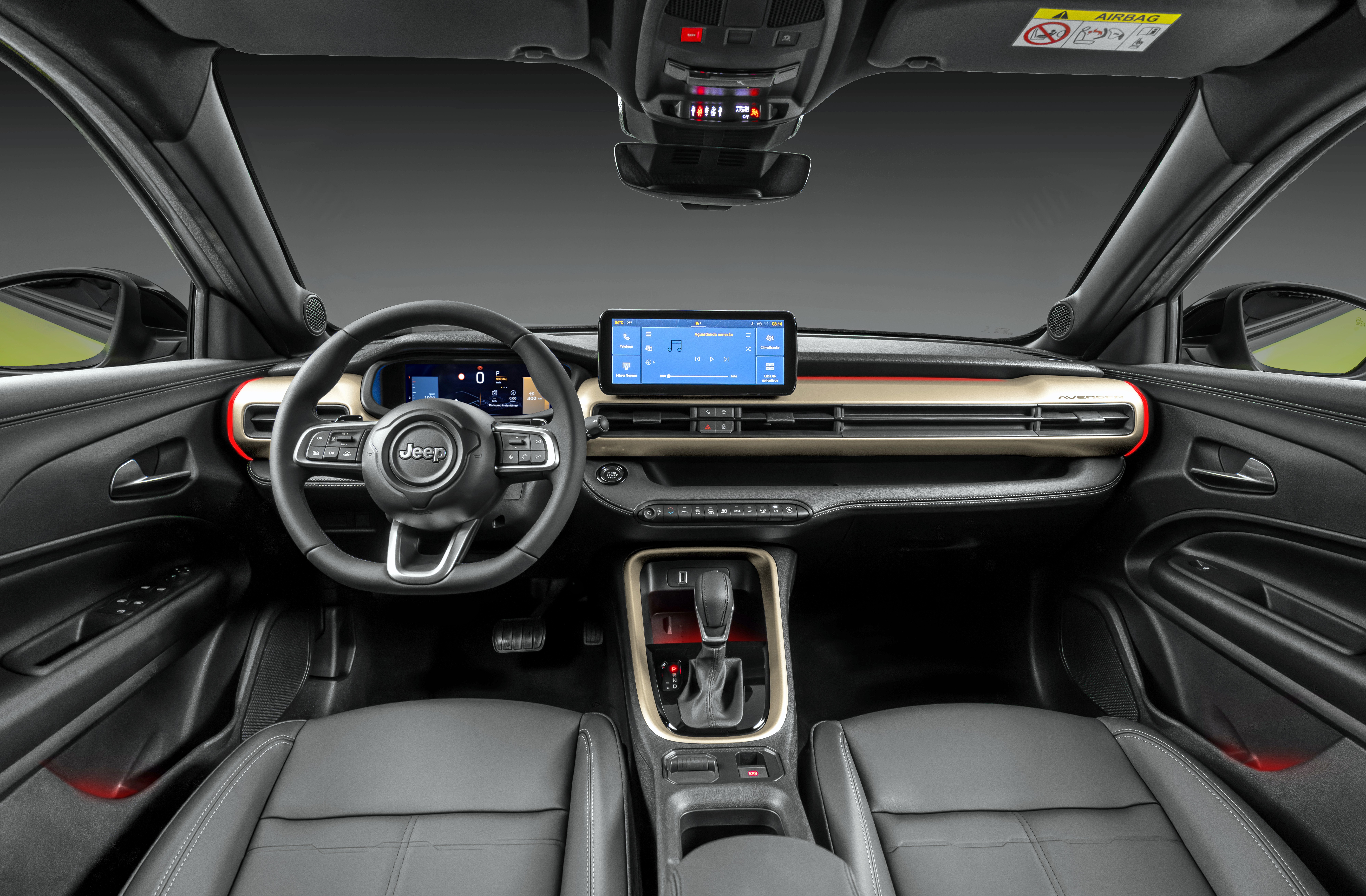 Interior de um carro Jeep com bancos de couro cinza, volante multifuncional e painel com detalhes dourados. Uma tela central exibe um sistema de navegação e mídia, enquanto o console tem câmbio automático e porta-objetos.
