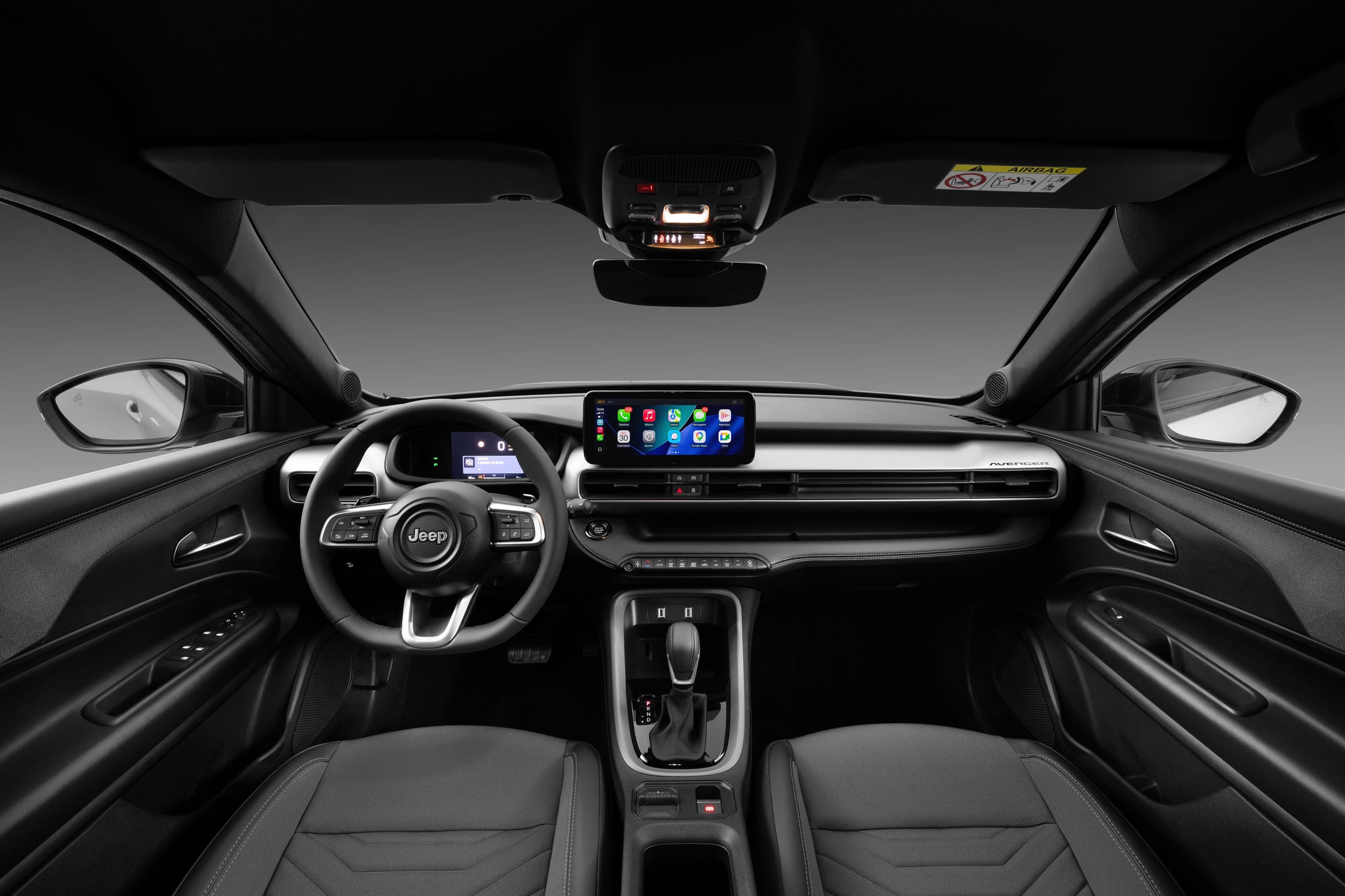 Interior de um carro Jeep com painel e bancos pretos, volante multifuncional com logo Jeep, tela multimídia central exibindo ícones de aplicativos e console com câmbio automático