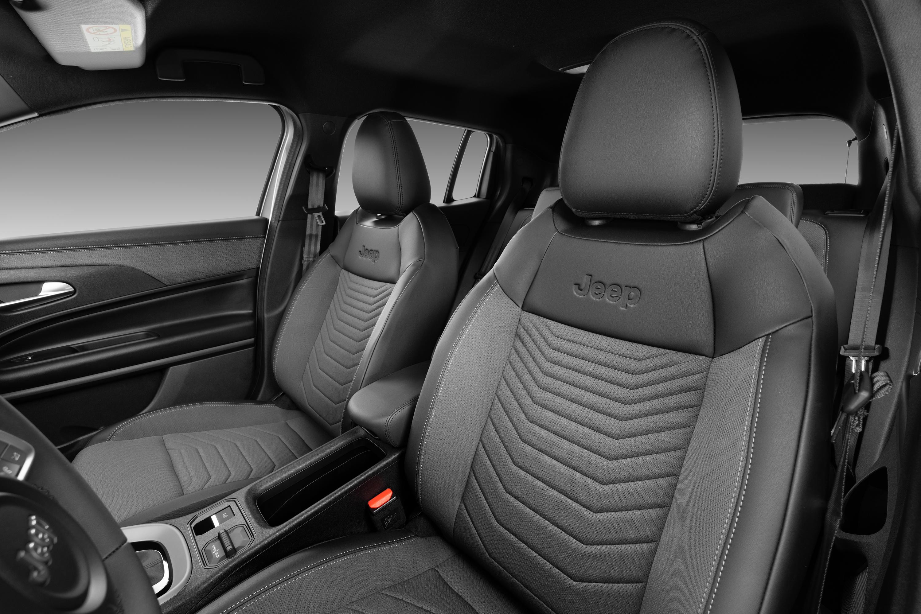 Interior de carro com bancos dianteiros em couro preto e cinza, com costuras e o logotipo Jeep bordado nos encostos de cabeça. O console central e o painel da porta também são visíveis, com detalhes em preto e cinza, e o volante parcialmente à esquerda