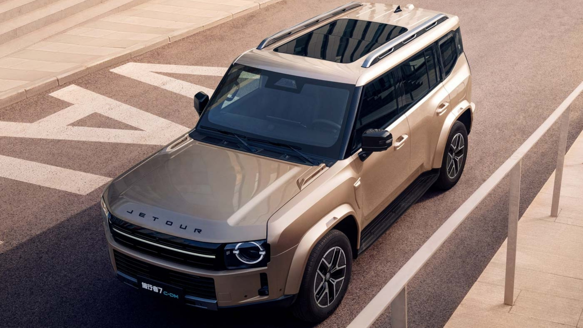 SUV Jetour Traveler dourado, visto de cima, estacionado em uma rua com faixas brancas e uma calçada clara com corrimão