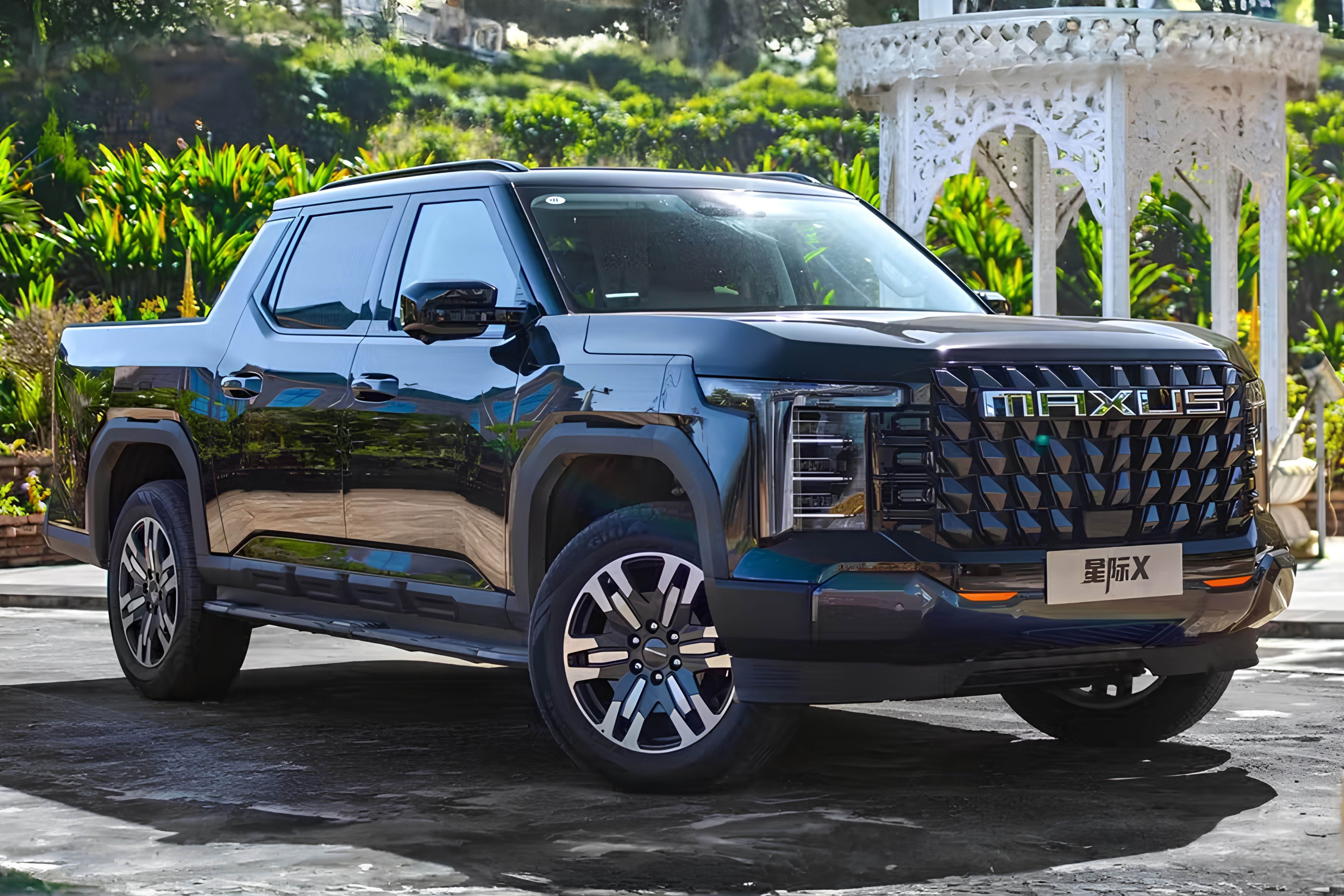 Picape Maxus preta brilhante, modelo 星际X, estacionada em uma área externa com vegetação exuberante e um gazebo branco ornamentado ao fundo