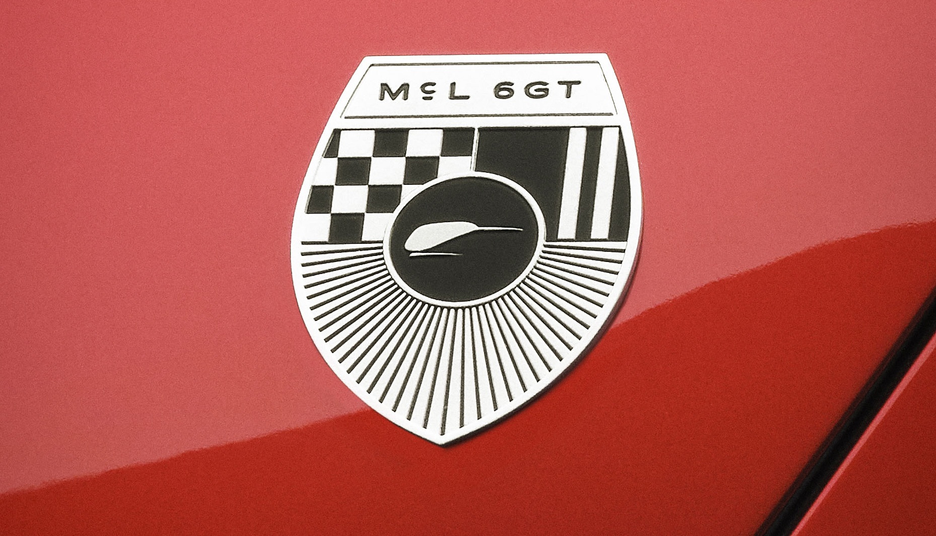 Emblema prateado e preto do carro M&L 6GT em formato de escudo, com um padrão xadrez, listras verticais e um desenho de um animal estilizado no centro, sobre uma superfície vermelha brilhante
