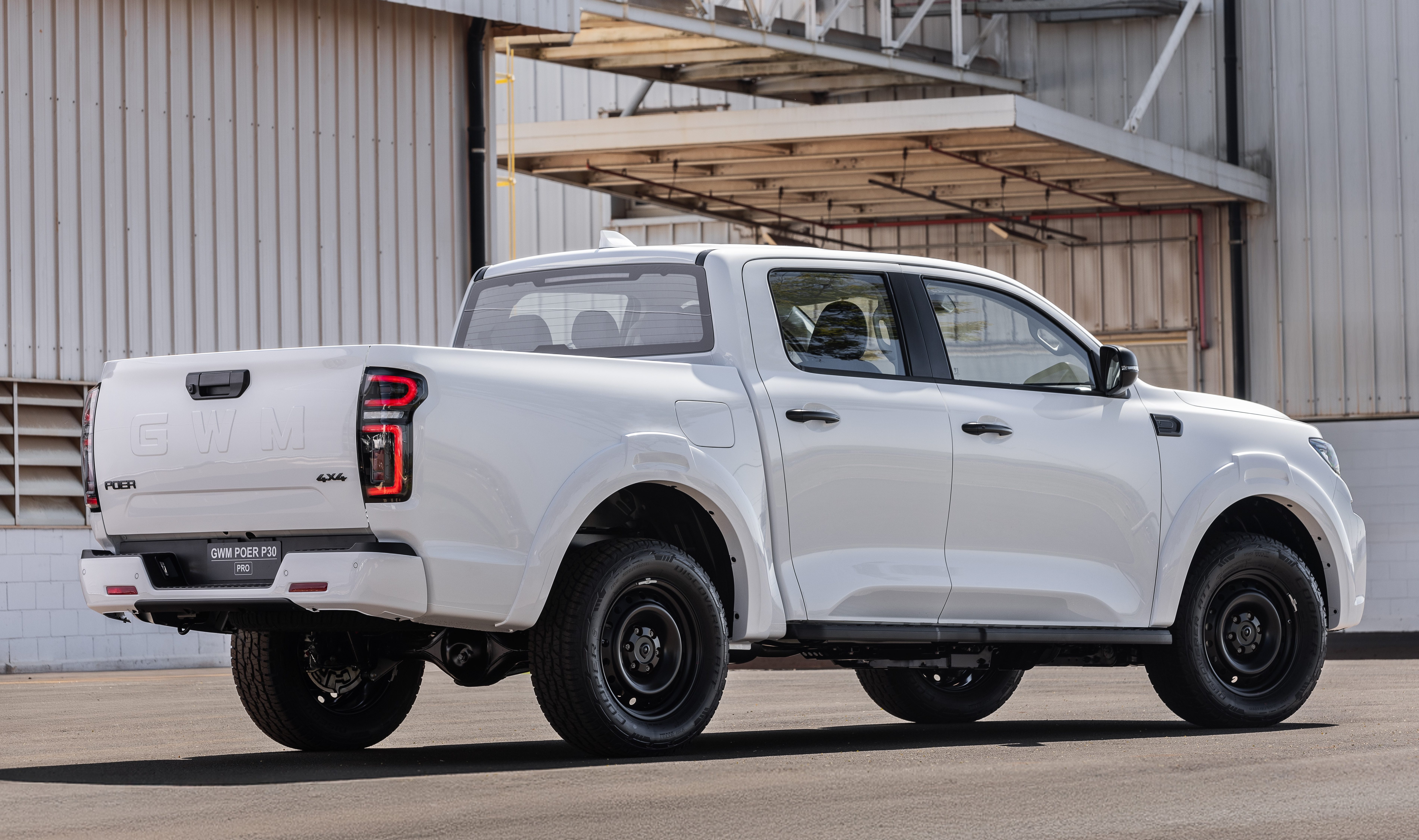Picape branca GWM Poer King Kong 4x4, vista de traseira e lateral, estacionada em pátio de concreto com um galpão cinza ao fundo