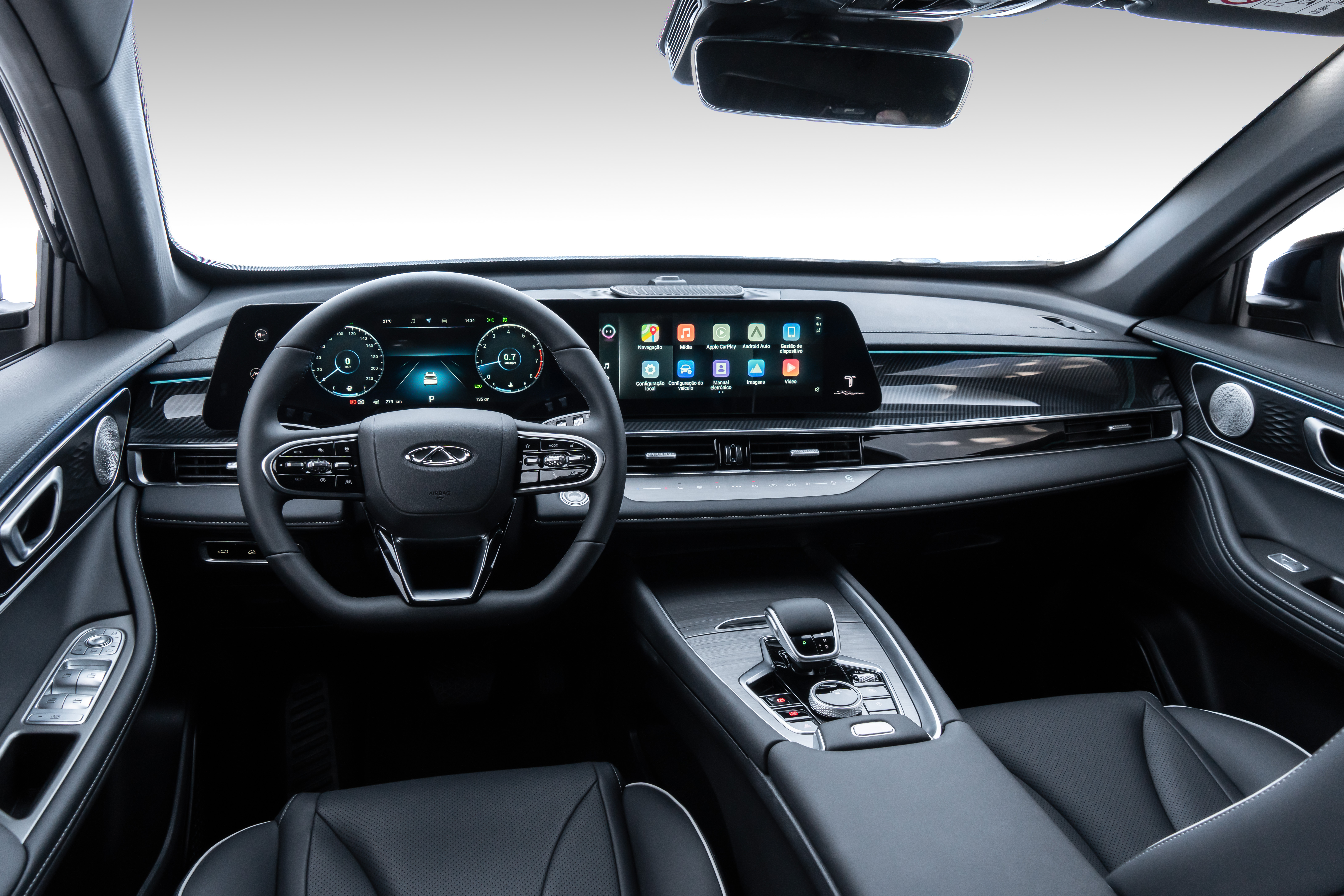 Interior de um carro moderno com volante multifuncional preto, painel digital e tela multimídia exibindo ícones de aplicativos. O console central tem acabamento metálico e seletor de marcha. Bancos de couro escuro e detalhes em azul claro nas portas e painel completam o design sofisticado