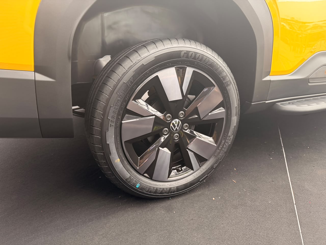 Roda de liga leve preta com detalhes polidos e pneu Goodyear de um carro amarelo, com parte do para-lama cinza escuro visível