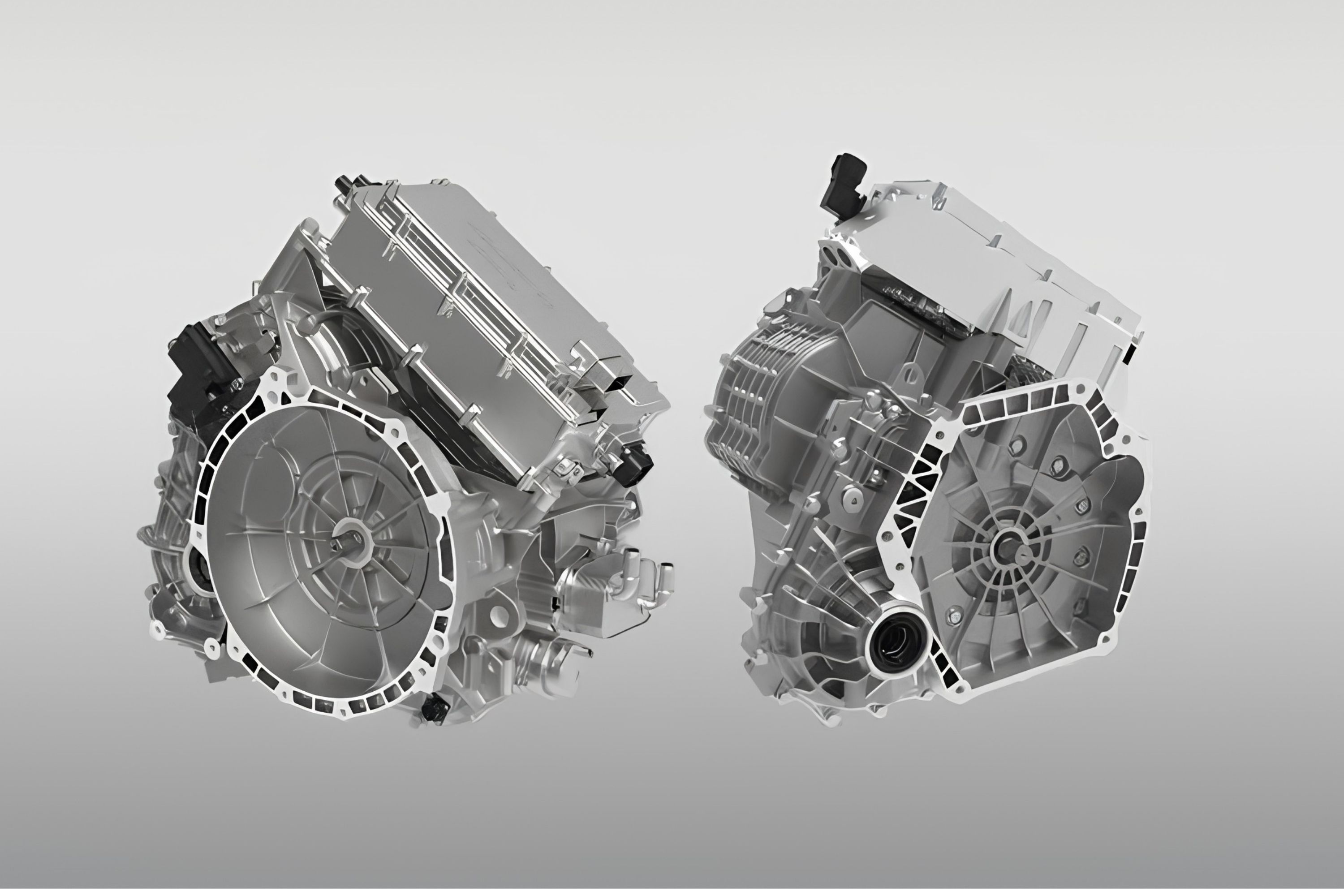 Duas unidades de transmissão automotiva prateadas, com detalhes em preto, exibidas em um fundo cinza claro. A unidade da esquerda está ligeiramente inclinada para a direita, e a da direita, para a esquerda, mostrando suas complexas estruturas internas e externas de metal.