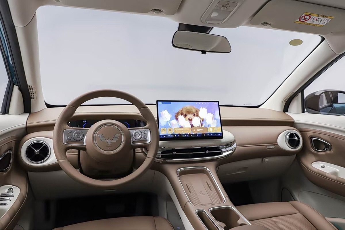Interior de um carro moderno com estofamento marrom e detalhes em branco. O volante tem um logotipo W estilizado. Uma tela multimídia exibe a imagem de um filhote de cachorro fofo entre flores brancas.