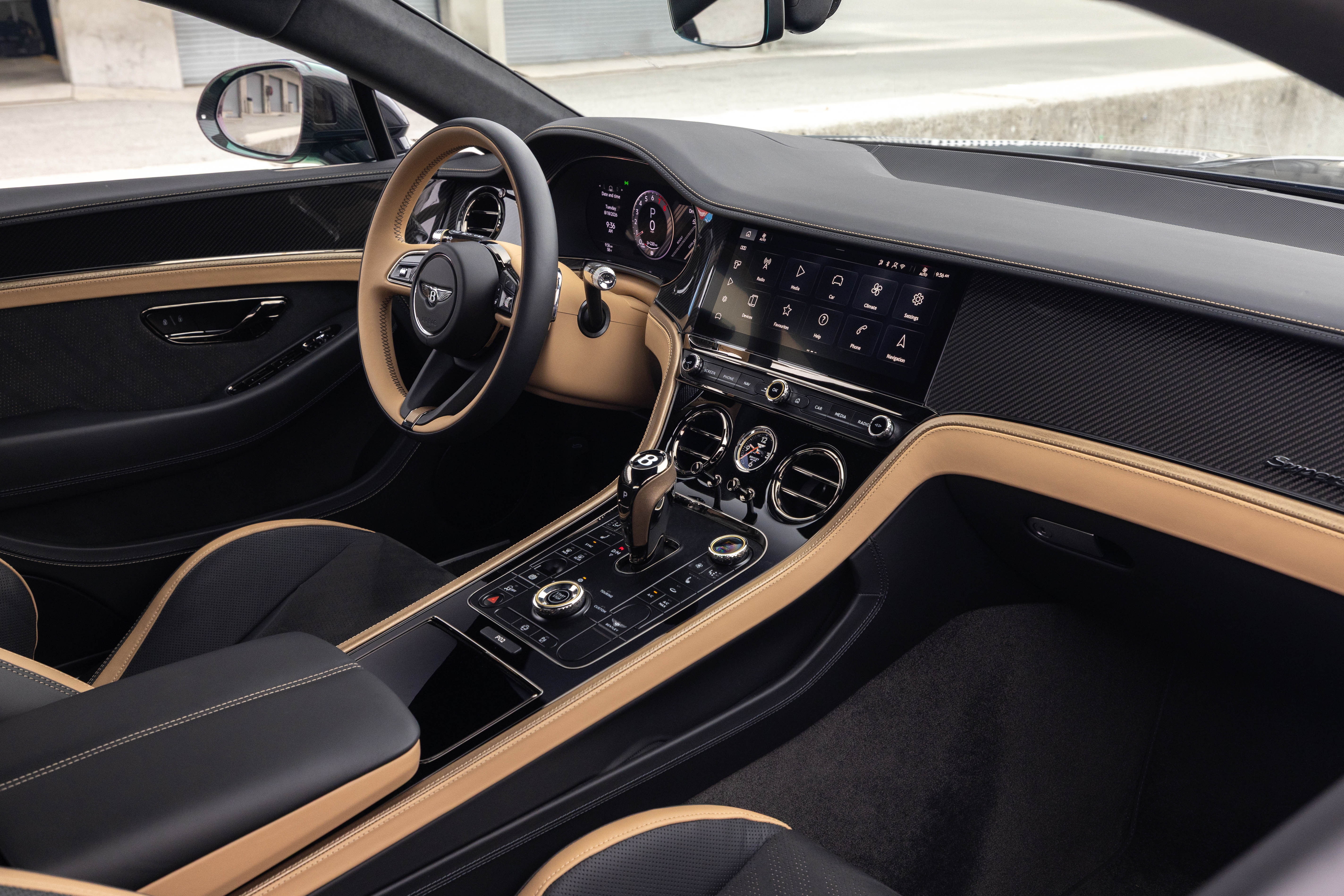 Interior de um carro de luxo com estofamento preto e detalhes em couro bege. O volante tem o centro preto e a borda bege. O painel possui uma tela multimídia grande, painel de instrumentos digital e saídas de ar cromadas. O console central exibe o câmbio e botões de controle.