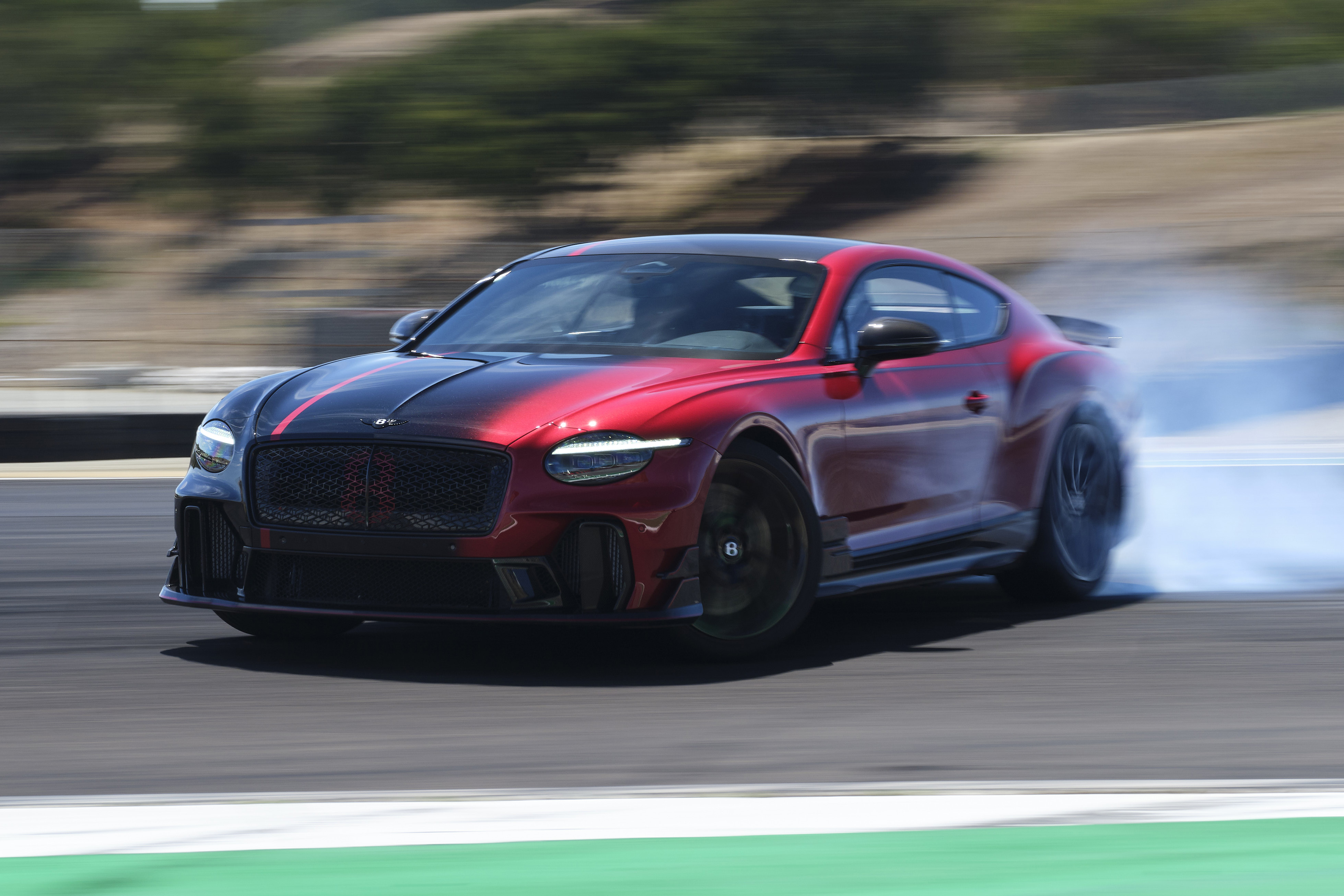Carro esportivo vermelho e preto em alta velocidade, derrapando e soltando fumaça dos pneus em uma pista de corrida, com o fundo borrado pelo movimento