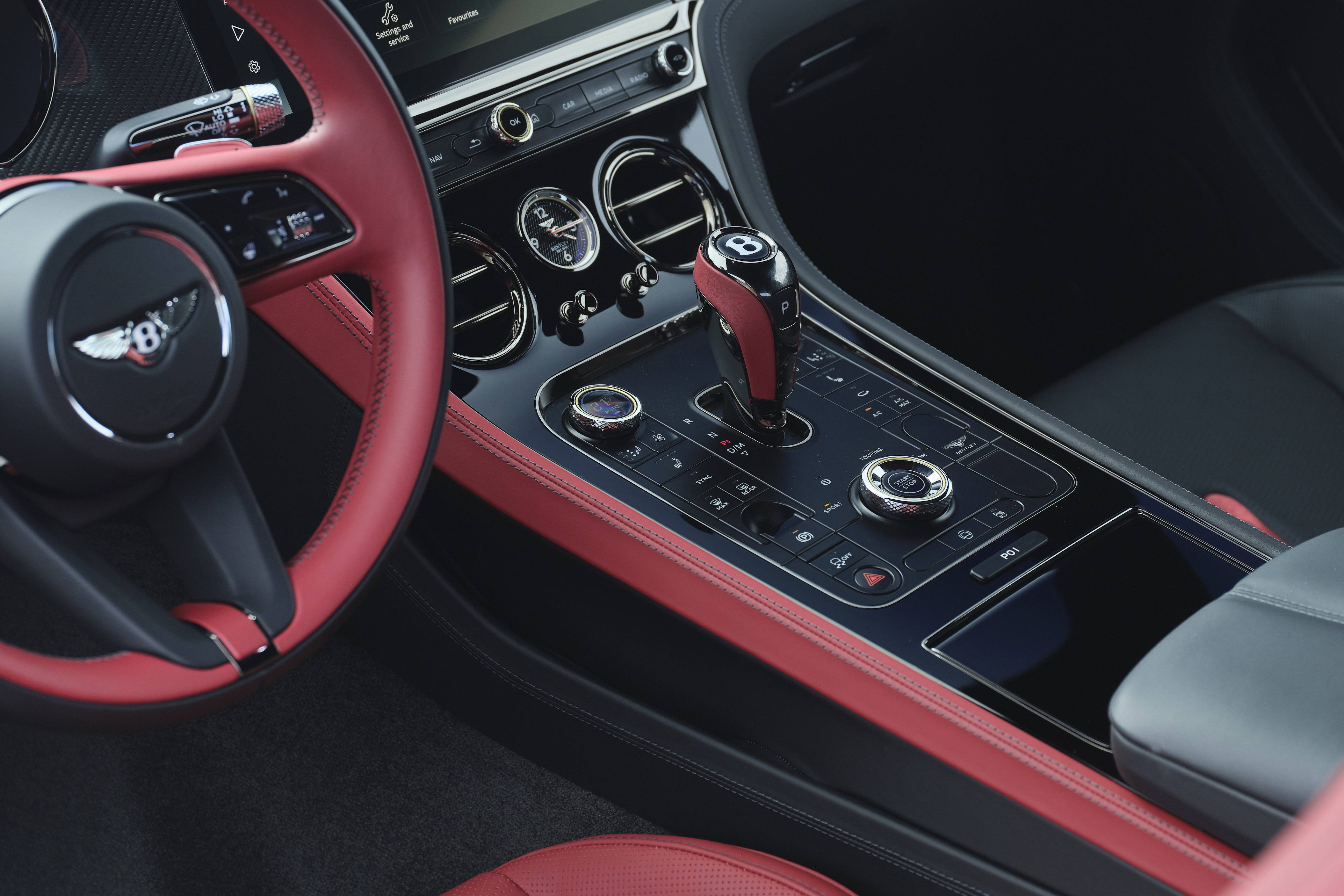 Interior de um carro de luxo com volante e detalhes em couro vermelho, painel central preto brilhante, câmbio e botões cromados