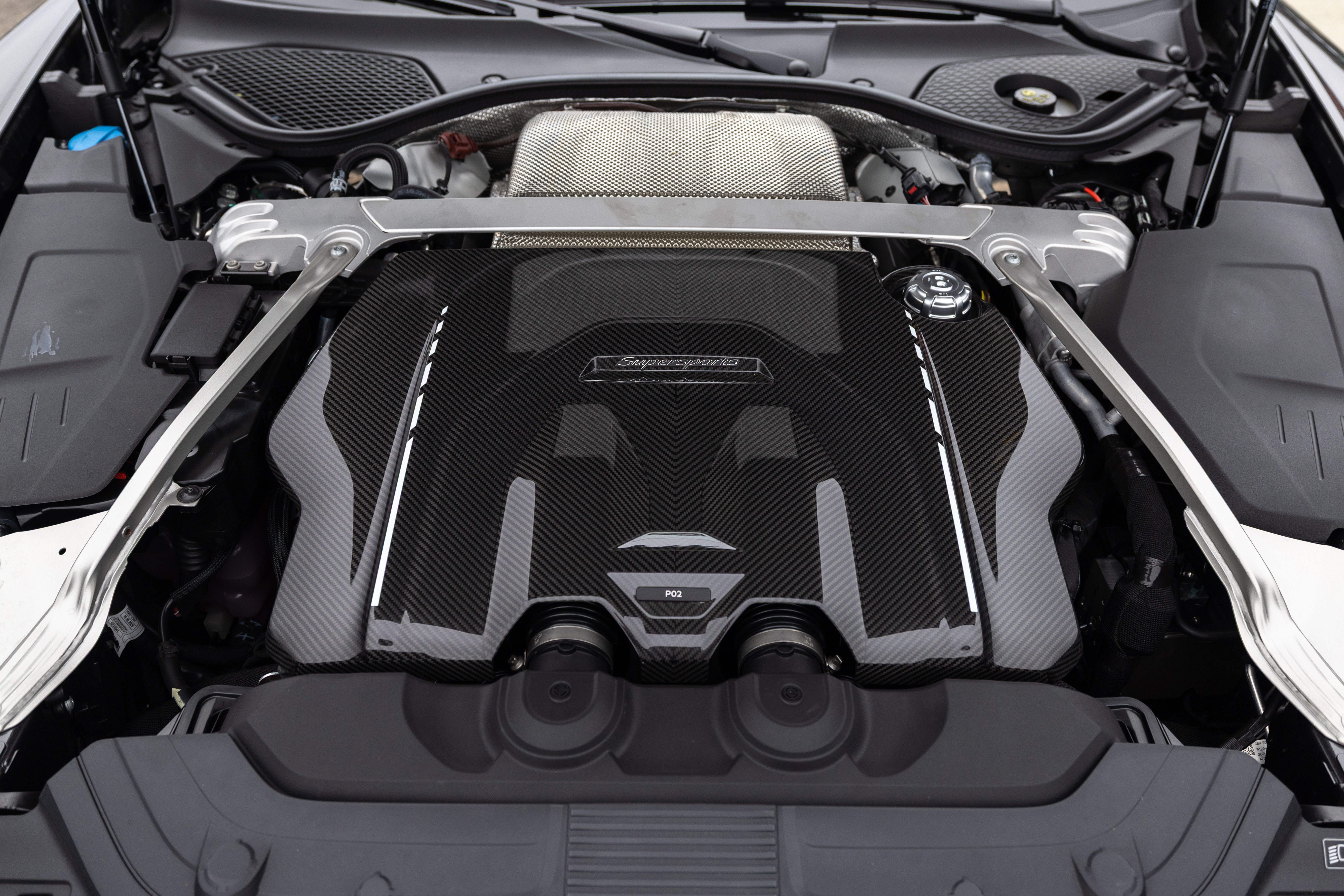 Motor de carro esportivo com tampa de fibra de carbono preta e detalhes prateados, exibindo a inscrição Superleggera