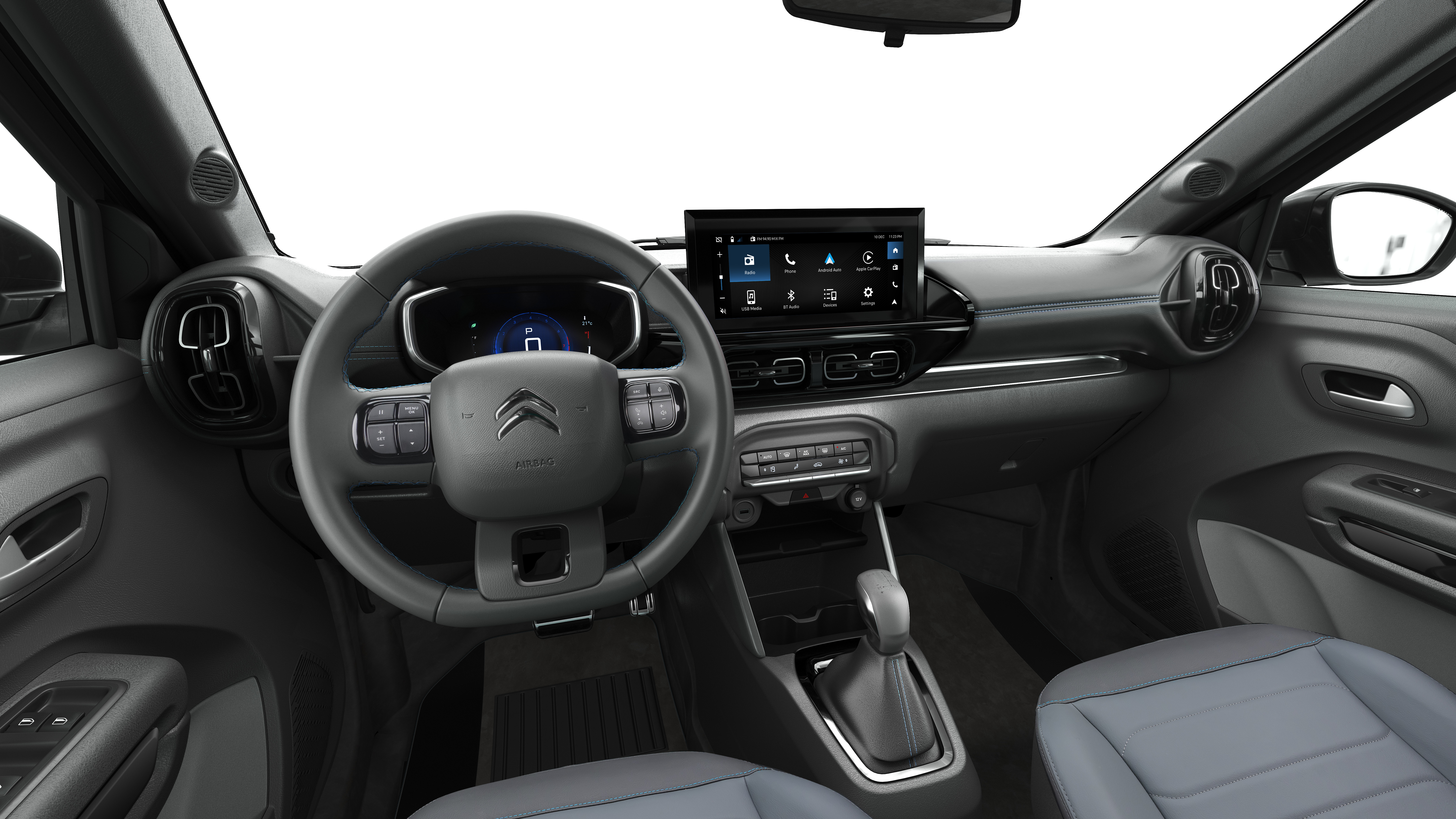 Interior de um carro moderno, com volante multifuncional cinza escuro e o logotipo da Citroën ao centro. O painel possui uma tela multimídia sensível ao toque exibindo ícones de aplicativos, e logo abaixo, botões de controle. O câmbio automático está visível no console central. Os bancos são cinza claro, e o ambiente geral é de um veículo novo e tecnológico