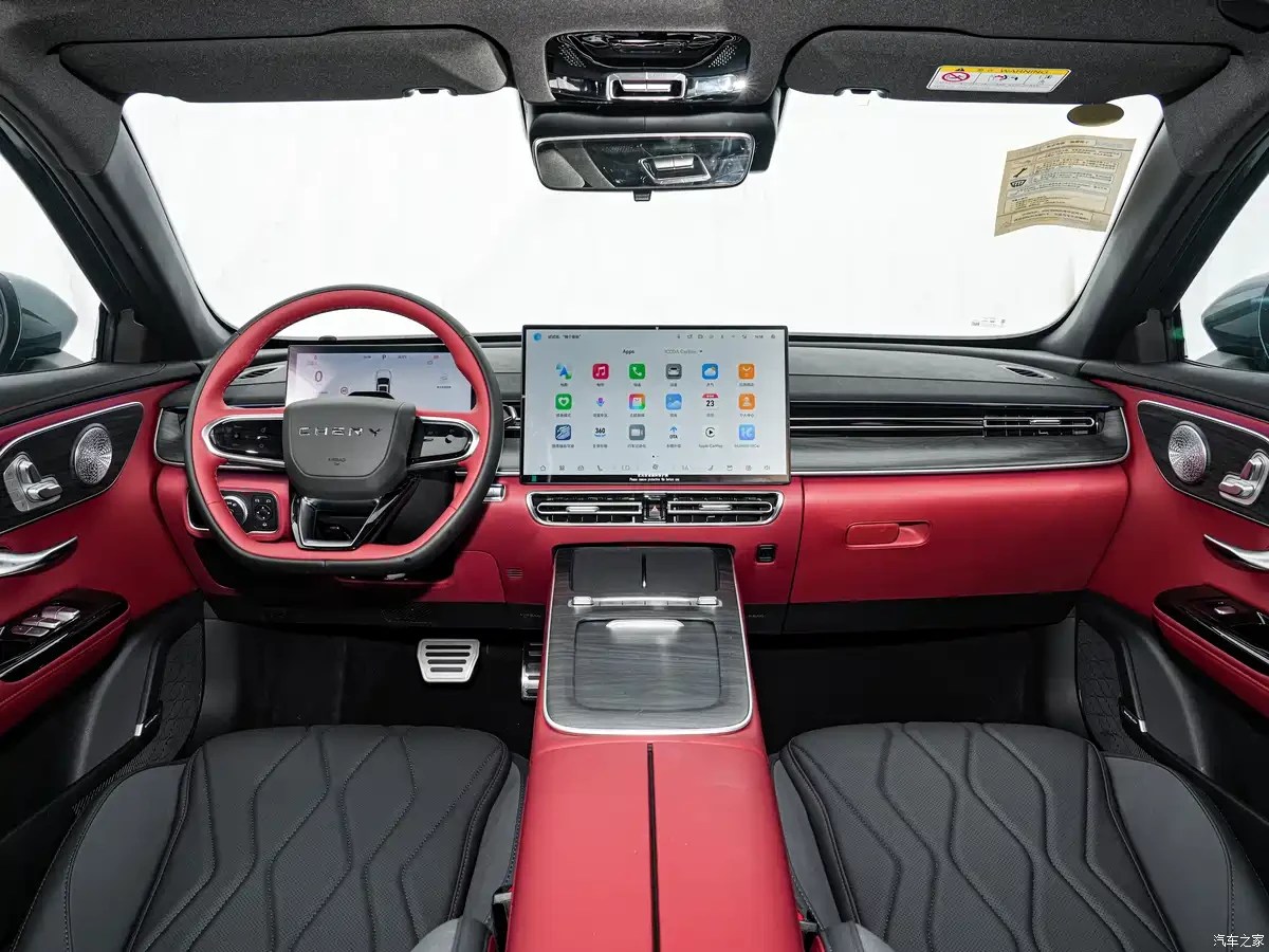 Interior de carro moderno com painel e volante em vermelho vibrante, bancos pretos com costura em losango. Uma tela grande central exibe ícones de aplicativos, e o volante tem o logo CHERY