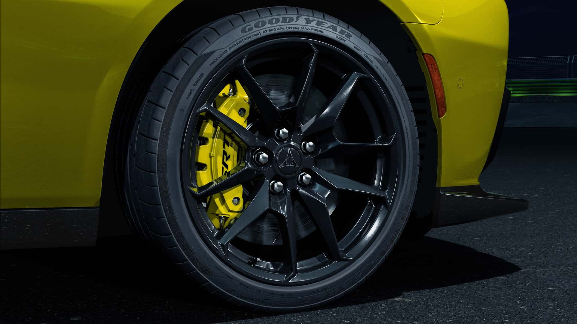 Roda preta de liga leve com múltiplos raios e pneu Goodyear, freio a disco amarelo brilhante, parte da lateral amarela de um carro esportivo