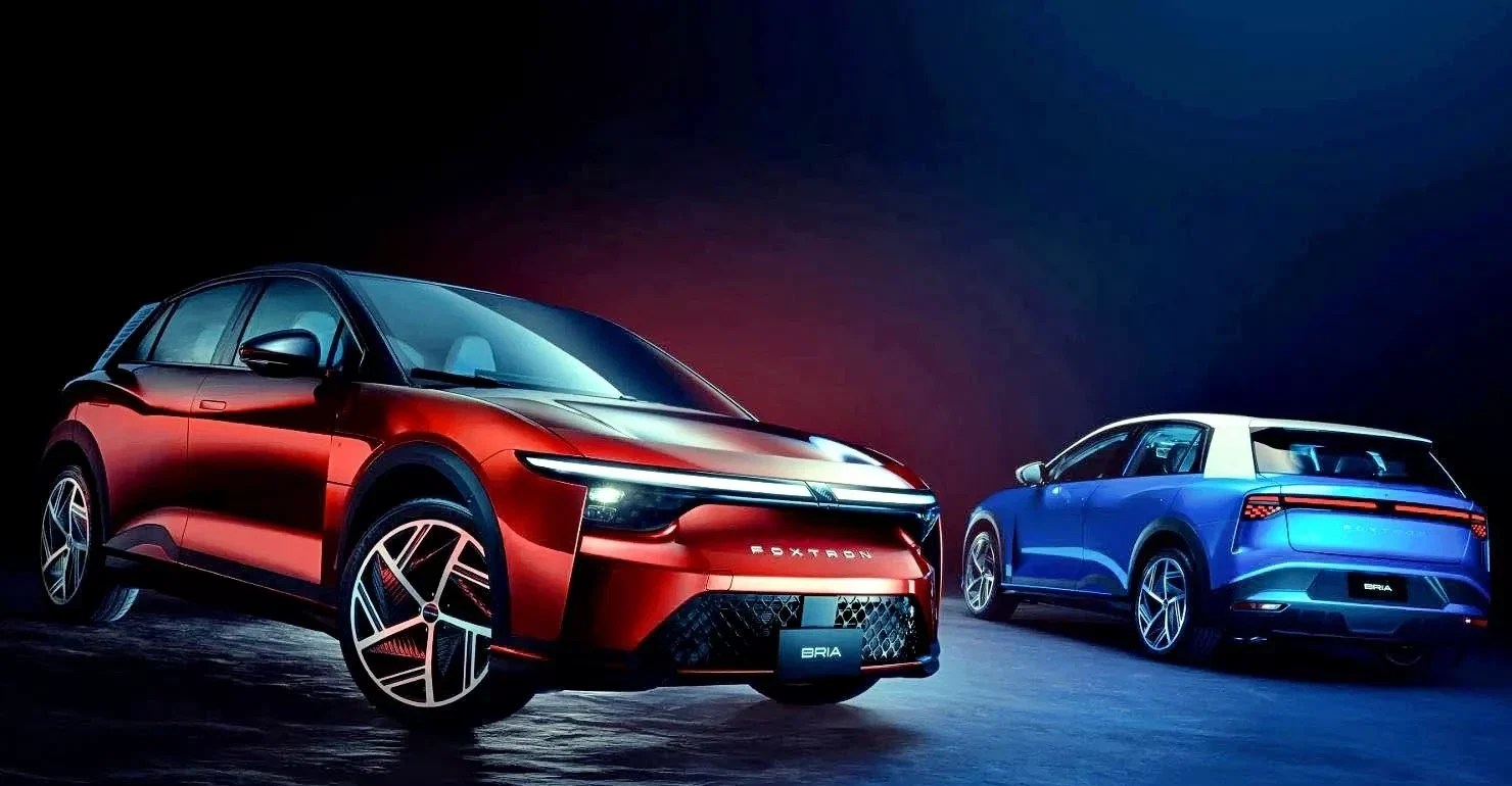 Dois carros elétricos modernos em um estúdio escuro: um SUV vermelho-escuro em primeiro plano, com faróis acesos e a marca FOXTRO na grade, e um SUV azul com teto branco ao fundo, visto de traseira