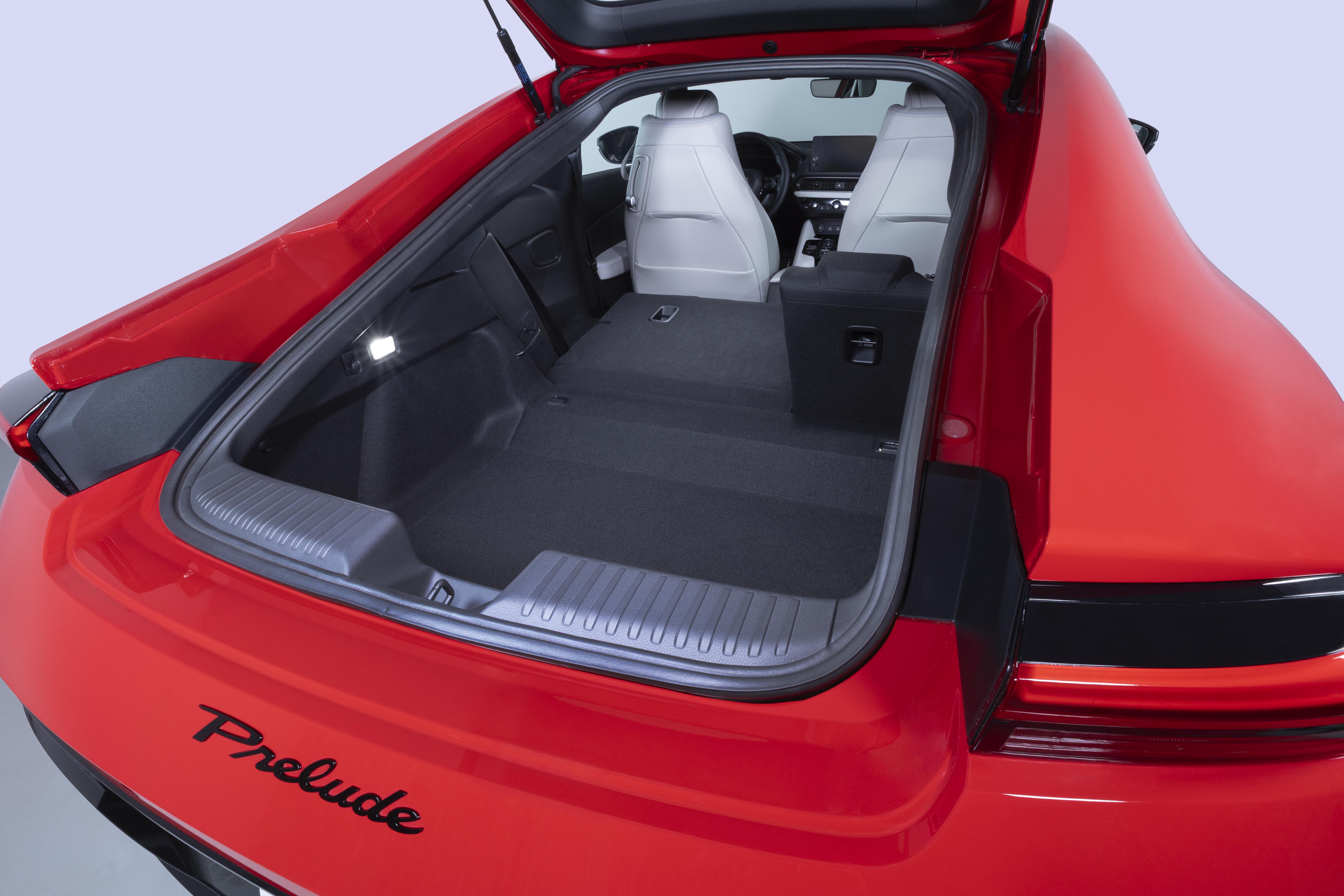 Traseira de um carro esportivo vermelho com a tampa do porta-malas aberta, revelando um interior espaçoso com bancos traseiros rebatidos e bancos dianteiros claros visíveis ao fundo. O nome Prelude está escrito em preto na parte inferior da tampa