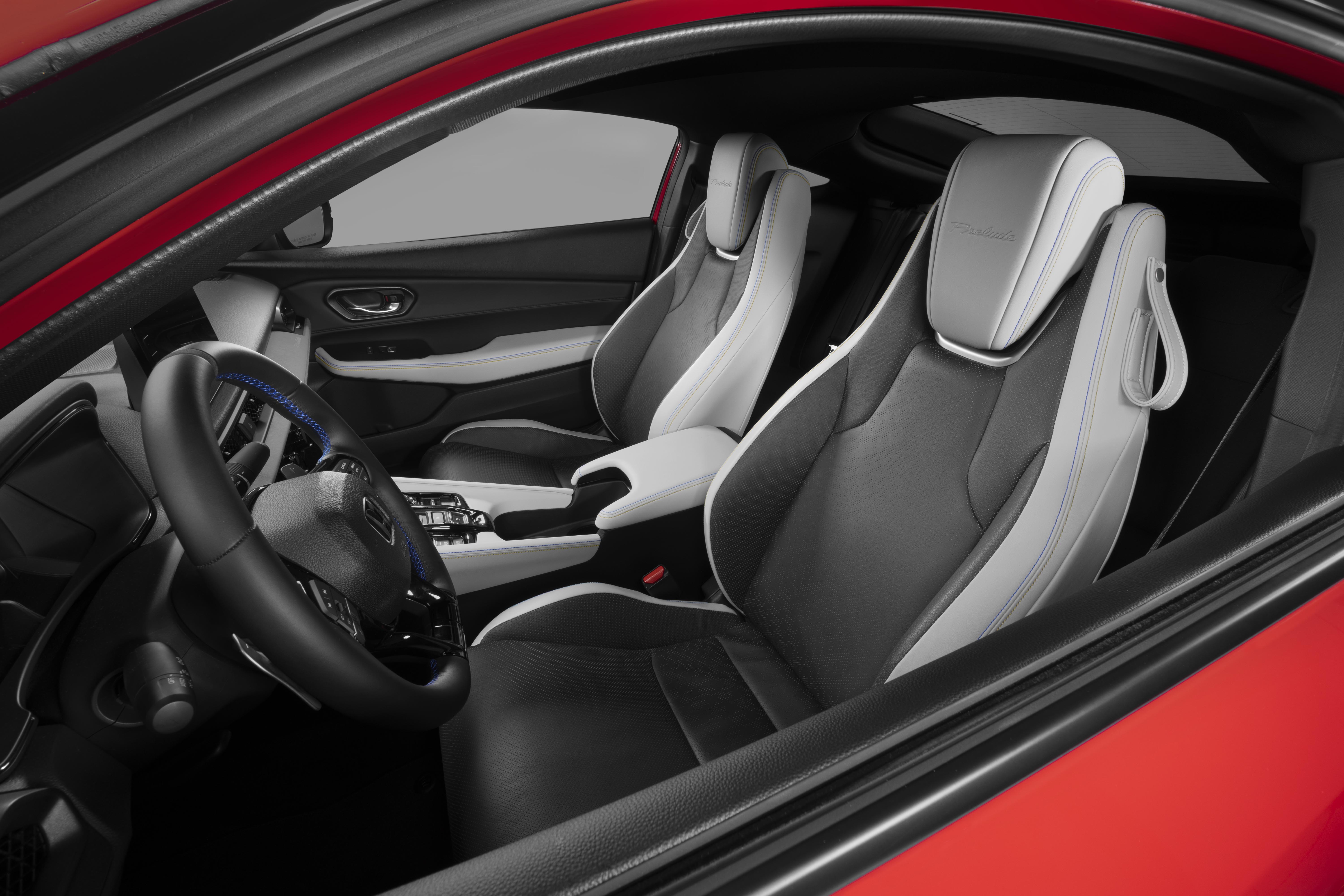 Interior de um carro esportivo vermelho, mostrando o volante escuro com costura azul e os bancos dianteiros em couro cinza e branco, com detalhes de alça nos encostos de cabeça
