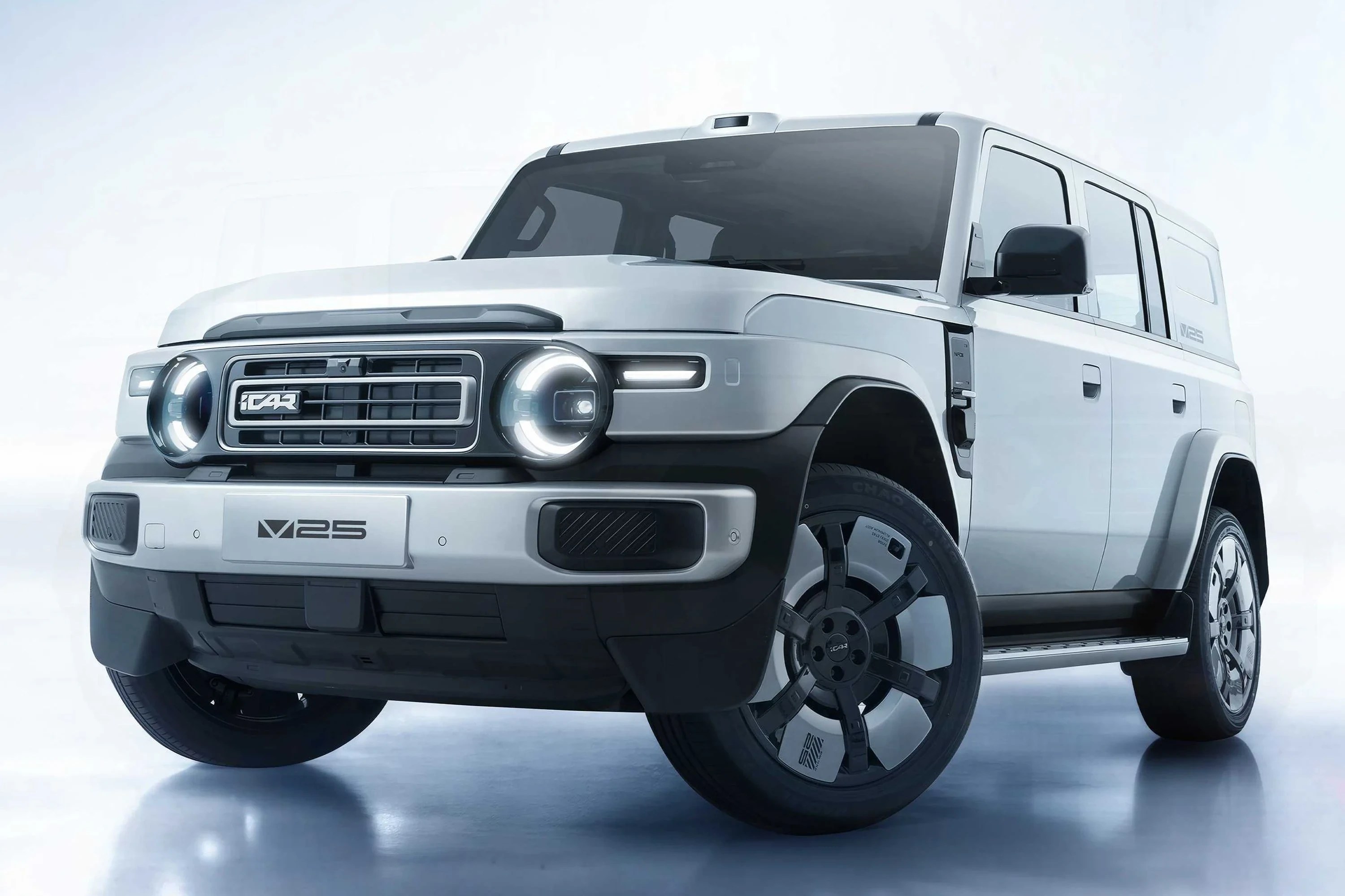 SUV elétrico iCAR V23 prateado, com design robusto e moderno, faróis redondos acesos e grade frontal com o logo iCAR, exibido em um estúdio com fundo claro e reflexo no chão