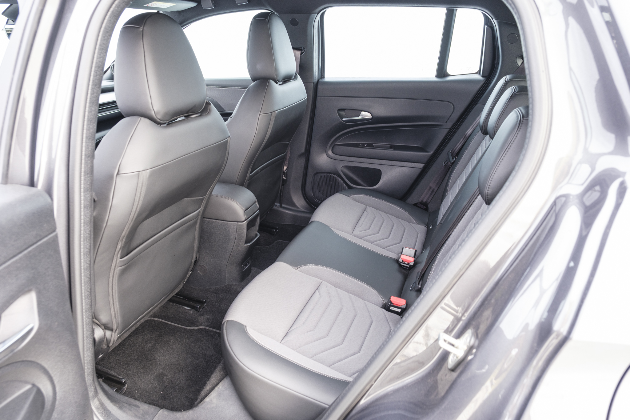 Interior de um carro com bancos traseiros em cinza claro e escuro, com detalhes em couro preto e tecido texturizado. Os bancos dianteiros, vistos por trás, são pretos. O console central tem porta-objetos. As janelas mostram um fundo claro