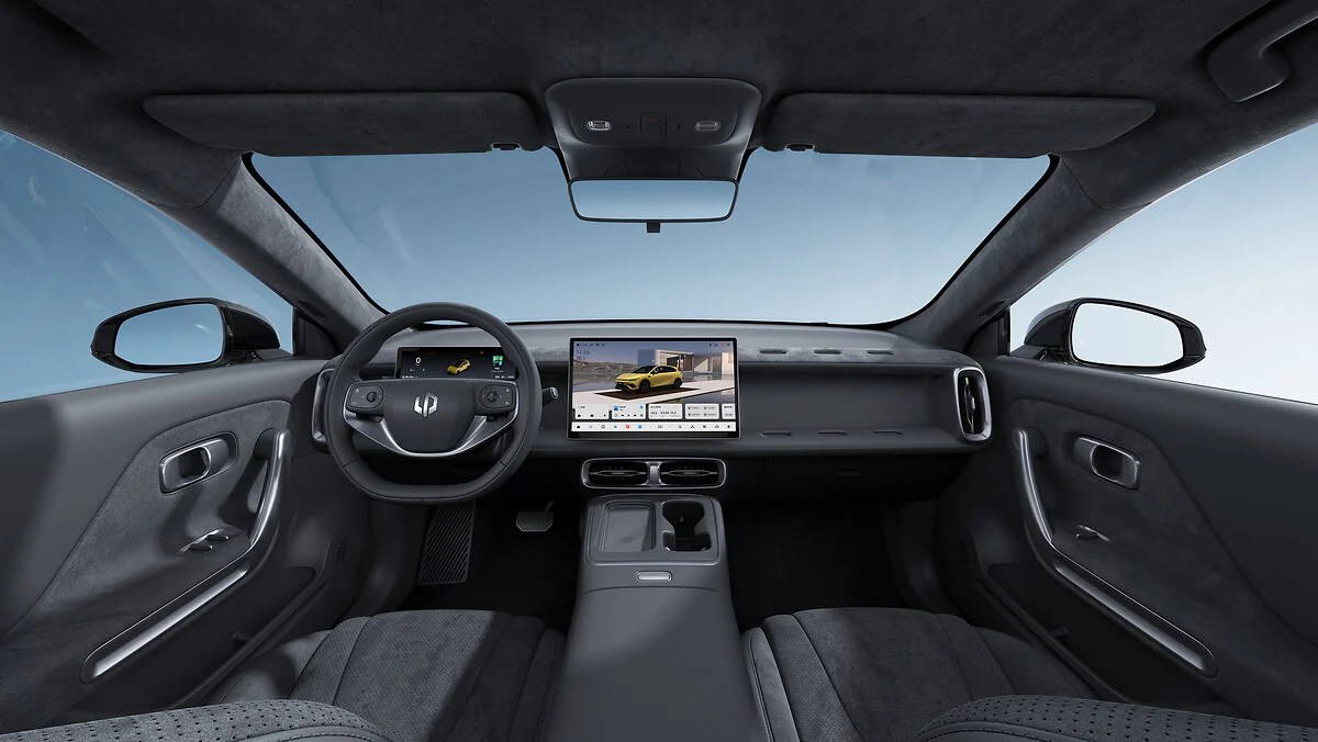 Interior moderno de um carro elétrico com painel escuro, volante multifuncional e uma tela central grande exibindo um SUV amarelo. O console central tem porta-copos e carregador sem fio. O para-brisa mostra um céu azul claro
