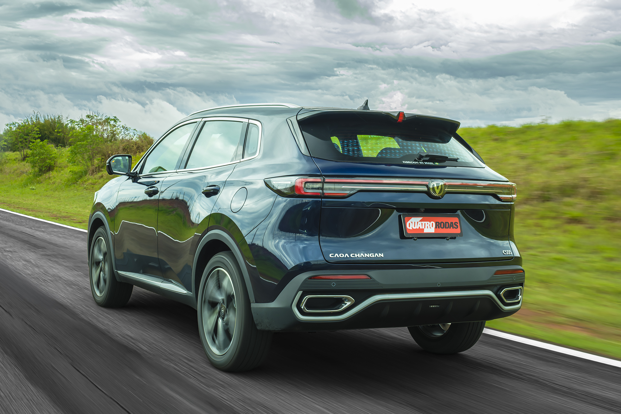 SUV escuro CAOA Changan em movimento, visto por trás, em uma estrada com vegetação verde e céu nublado