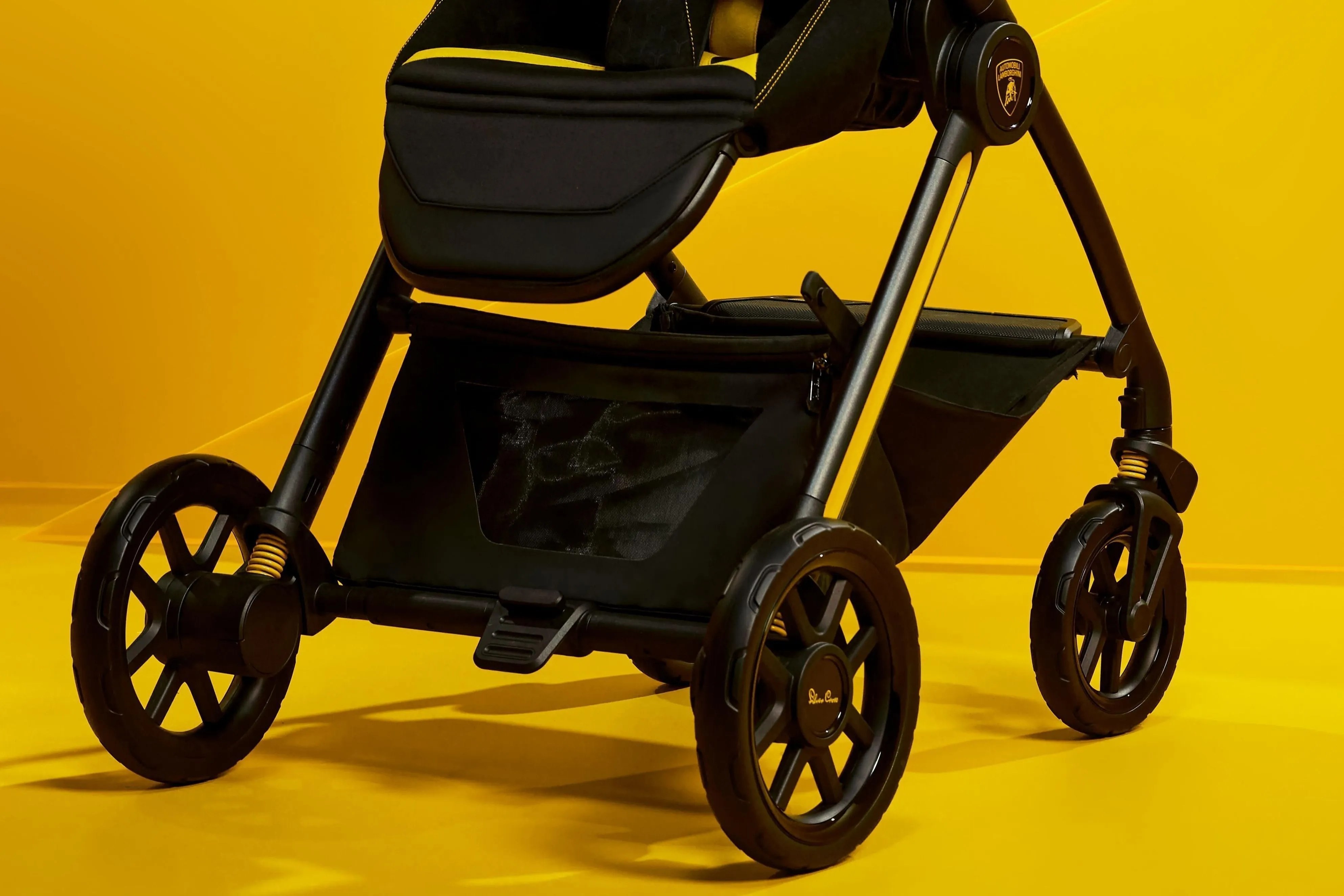 Carrinho de bebê preto com detalhes amarelos, estrutura metálica e rodas pretas, em um fundo amarelo vibrante
