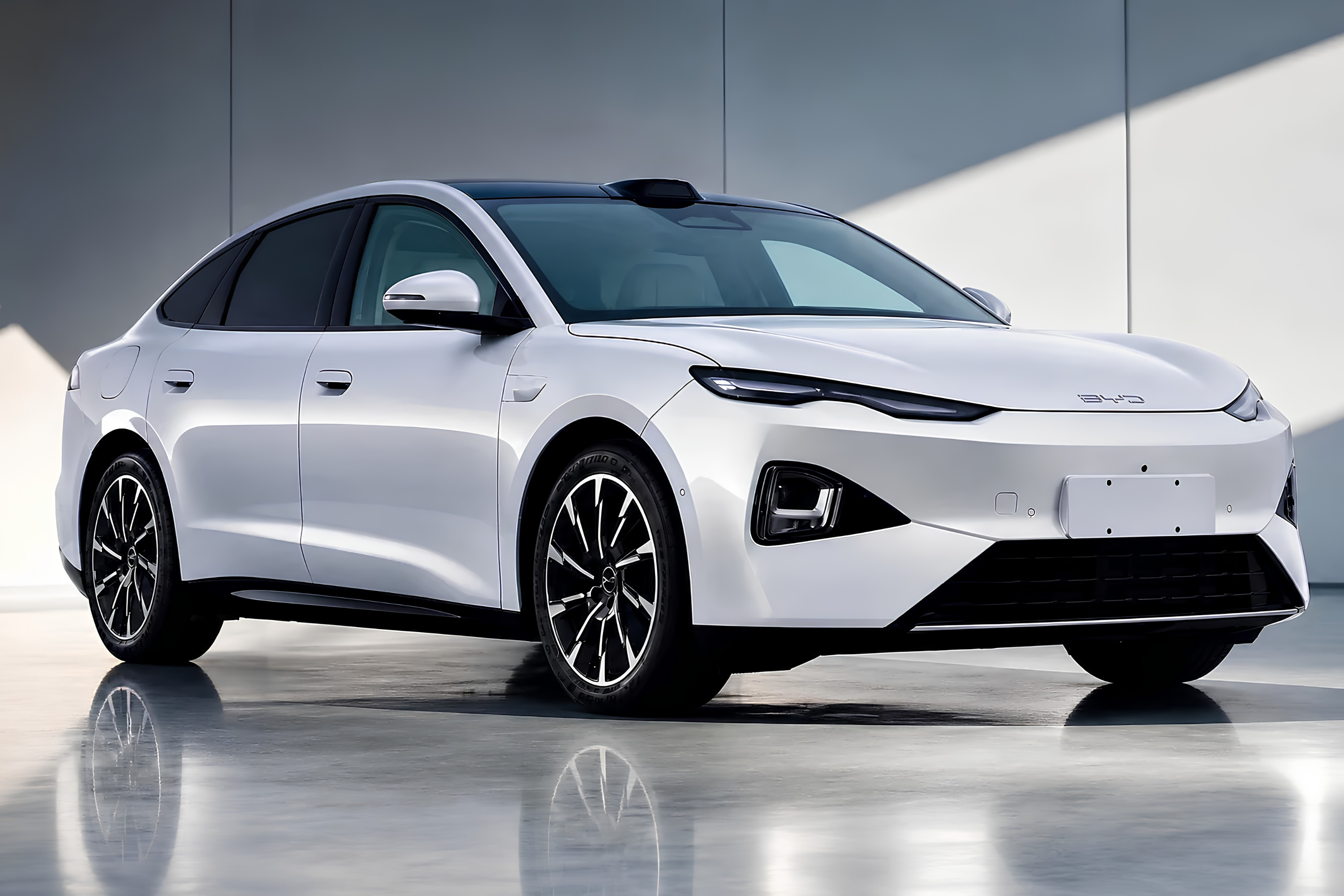 Carro elétrico BYD Seal branco perolado, com teto preto, estacionado em um ambiente moderno com paredes claras e piso reflexivo. O veículo tem design elegante, faróis finos e rodas esportivas pretas com detalhes prateados