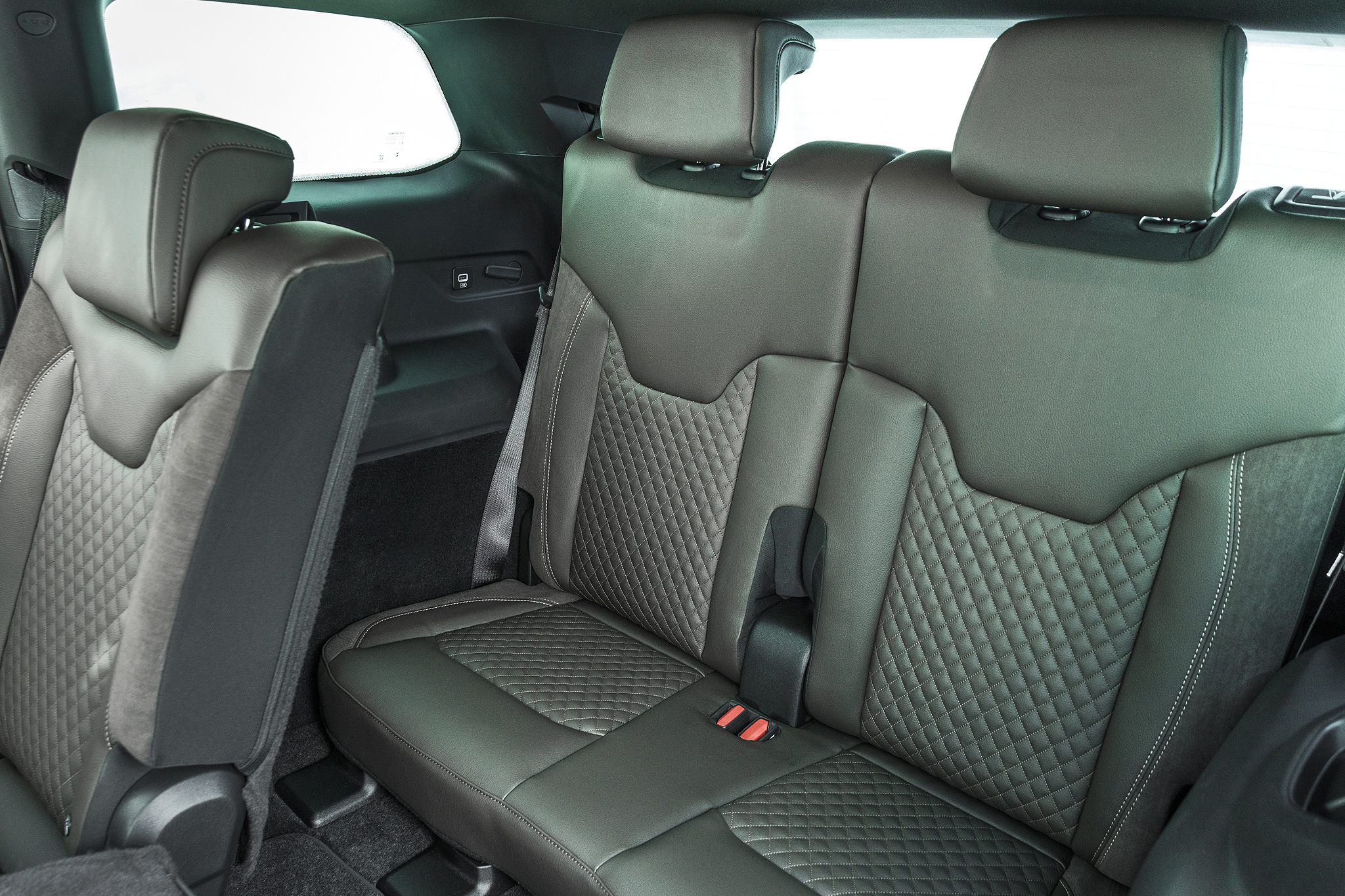 Interior de carro com bancos traseiros de couro marrom-escuro, com detalhes acolchoados em losangos. O banco da frente, à esquerda, está rebatido. Cintos de segurança cinzas e fivelas vermelhas são visíveis.