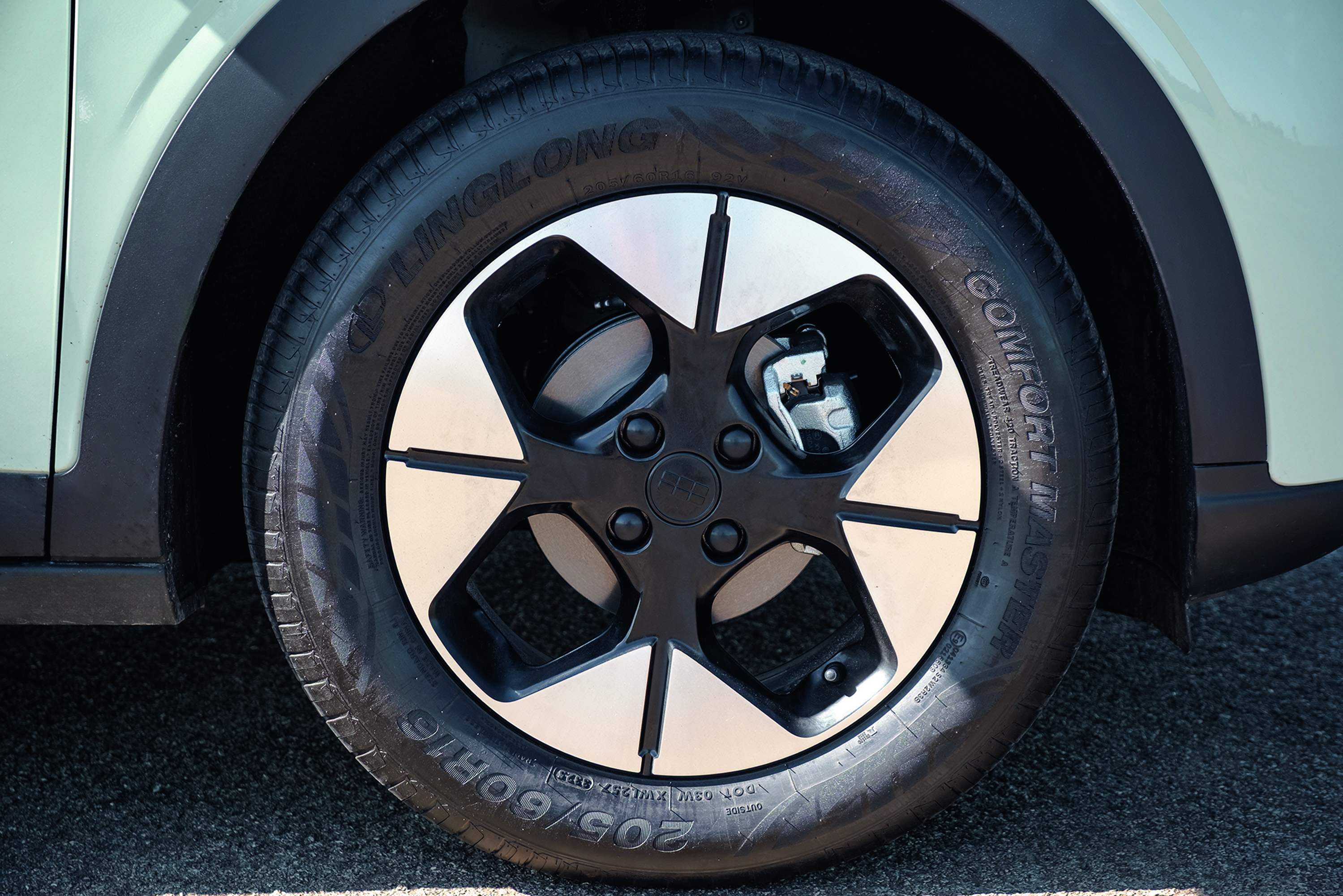 Pneu preto com aro de liga leve bicolor, preto e prata, em um carro verde-claro. O pneu tem a marca Linglong Comfort Master e a especificação 205/60R16 visíveis