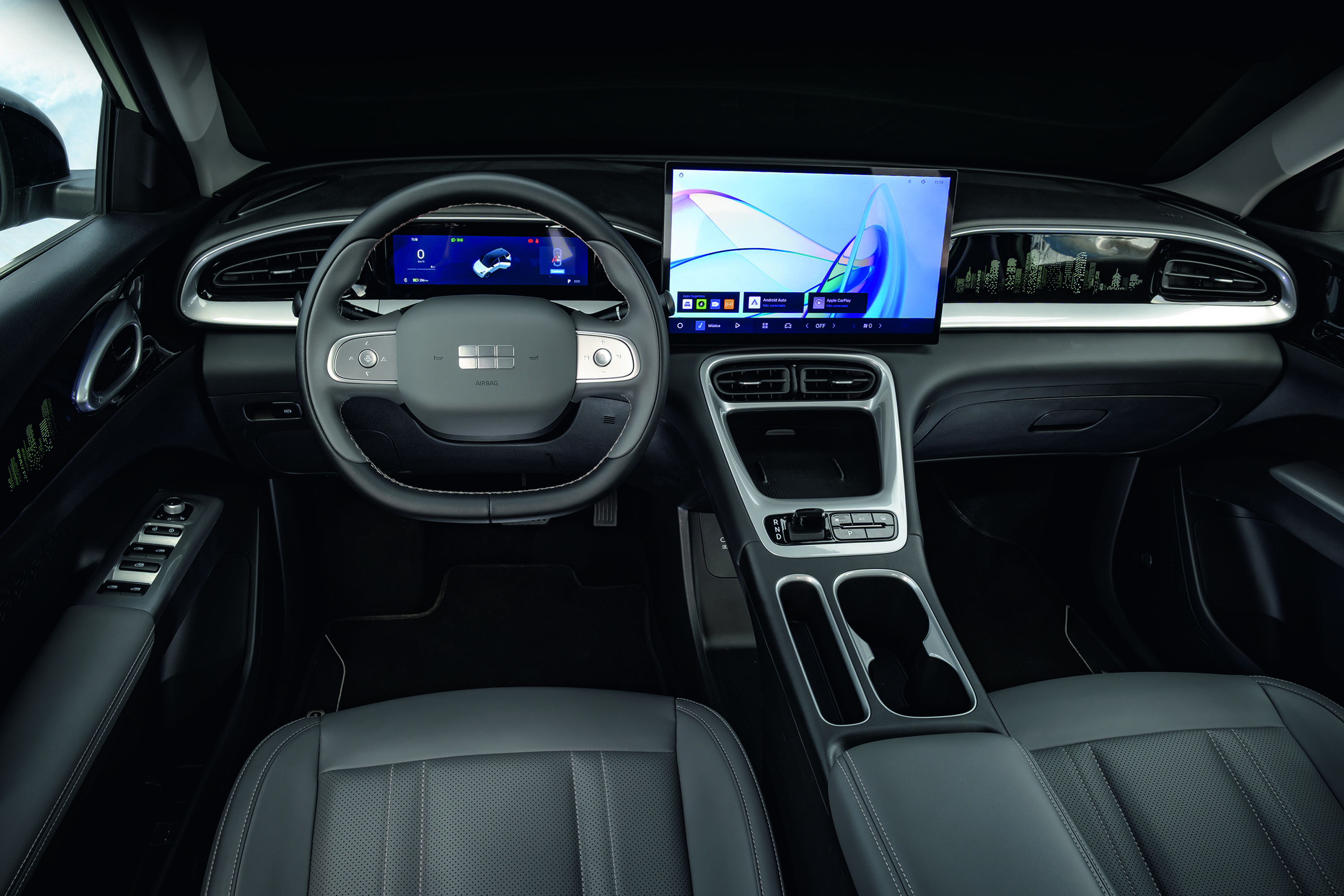 Interior de um carro moderno com volante cinza e tela digital no painel, exibindo um gráfico abstrato em tons de azul e roxo. O console central tem acabamento prateado e porta-copos. O estofamento dos bancos é preto com costuras claras