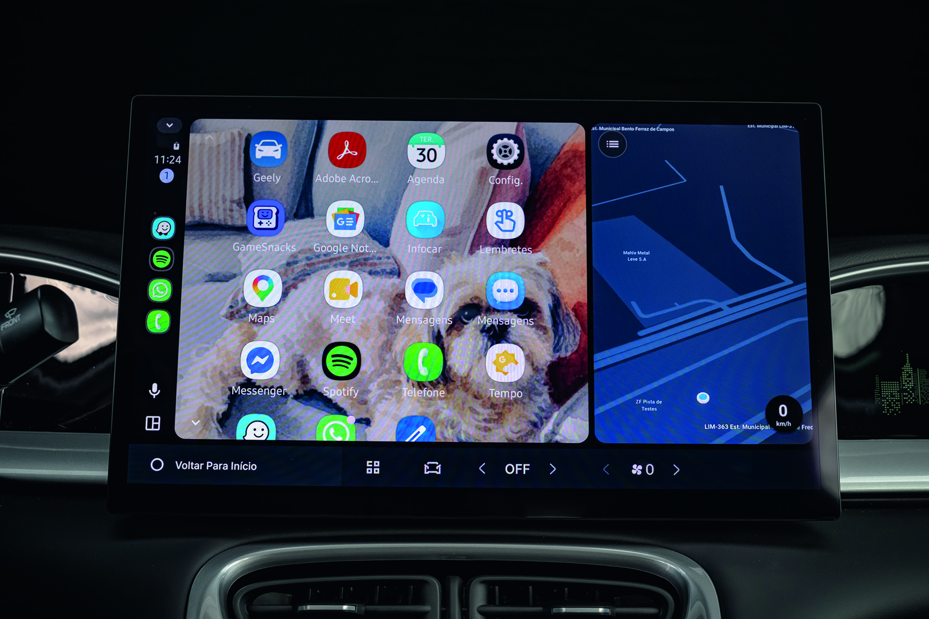 Tela multimídia de carro exibindo aplicativos e um mapa. À esquerda, um papel de parede com um cachorro shih-tzu e ícones de apps como Geely, Adobe Acrobat, Agenda, Config, GameSnacks, Google Not, Infocar, Lembretes, Maps, Meet, Mensagens, Mensagens, Messenger, Spotify, Telefone e Tempo. À direita, um mapa de navegação com rotas em azul escuro e claro. Na parte inferior da tela, botões de controle como Voltar Para Início, OFF e um velocímetro marcando 0