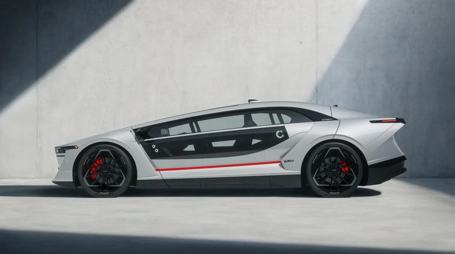 Carro conceito prateado com design futurista, perfil lateral, faixas vermelhas e pretas na parte inferior, rodas pretas com pinças de freio vermelhas, estacionado em ambiente minimalista com parede cinza e sombra diagonal