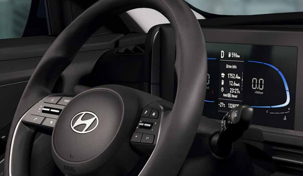 Interior de um carro Hyundai com volante preto e o logotipo da marca ao centro. À direita, um painel digital exibe informações de condução, como distância percorrida, consumo e tempo, com um velocímetro digital marcando 0.0