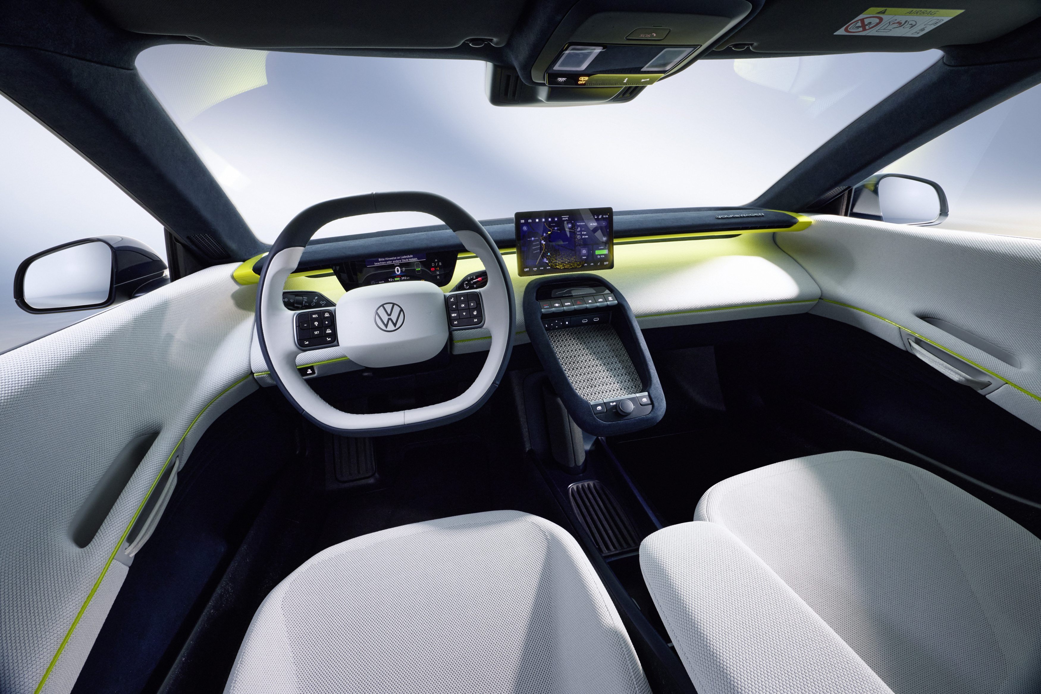 Interior de um carro moderno com volante branco e logo Volkswagen, painel digital e tela multimídia central. Bancos claros e detalhes em amarelo neon no acabamento, criando um ambiente futurista e minimalista