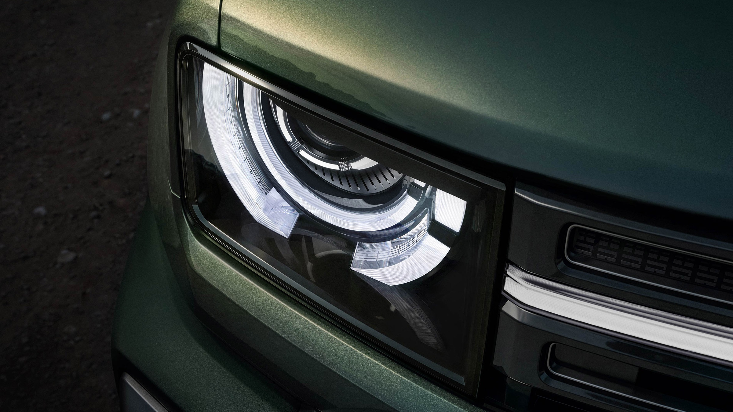Farol LED moderno de um carro verde-escuro, com luzes diurnas em formato de C e detalhes cromados na grade frontal