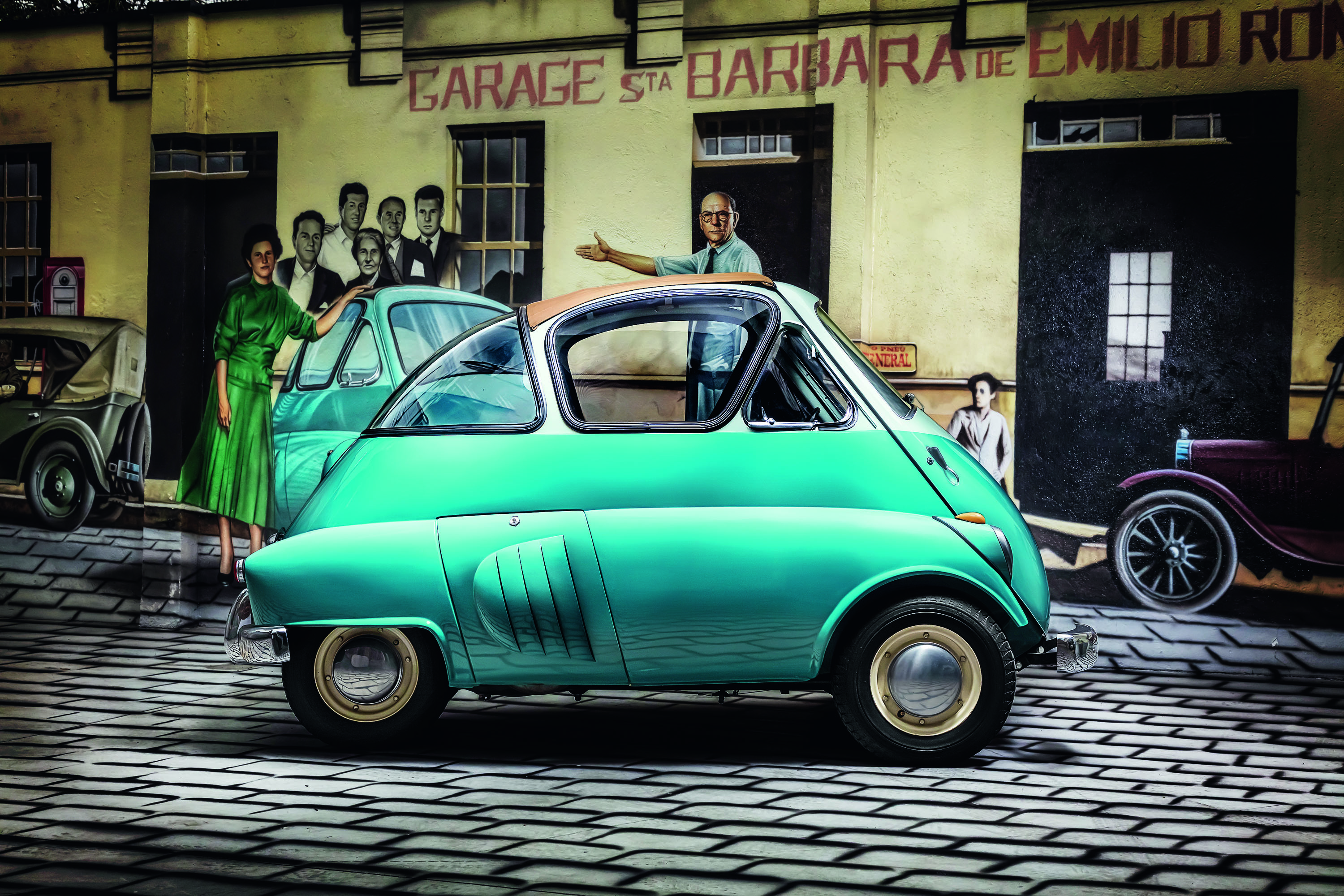 Pintura de um homem de camisa azul e calça cinza apontando para um carro verde-água com teto marrom, estacionado em uma rua de paralelepípedos. Ao fundo, uma mulher de vestido verde e um grupo de homens observam. A fachada de um prédio amarelo com a inscrição GARAGE STA BARBARA DE EMILIO ROM aparece atrás, com um carro antigo cinza à esquerda e um bordô à direita