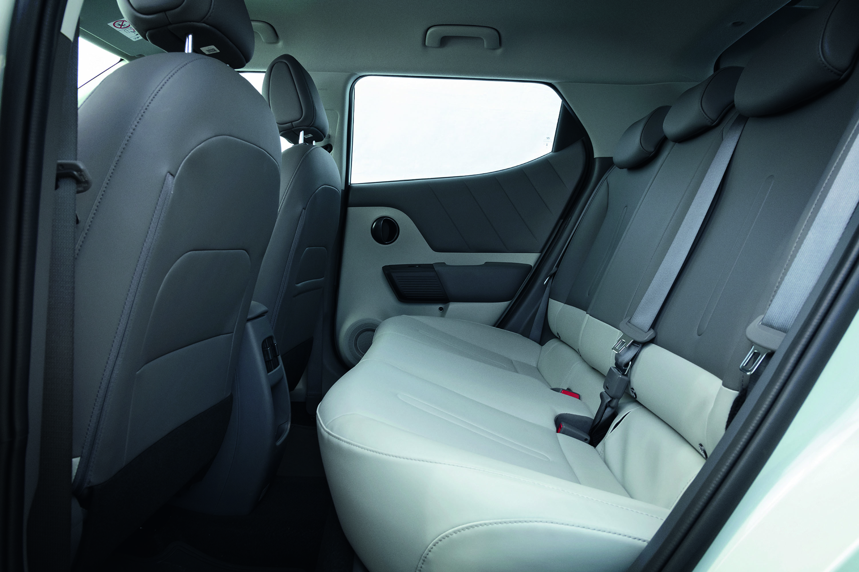 Interior de carro com bancos traseiros em dois tons, cinza escuro e claro, com cintos de segurança visíveis e encostos de cabeça. As portas têm acabamento cinza e uma janela lateral clara.