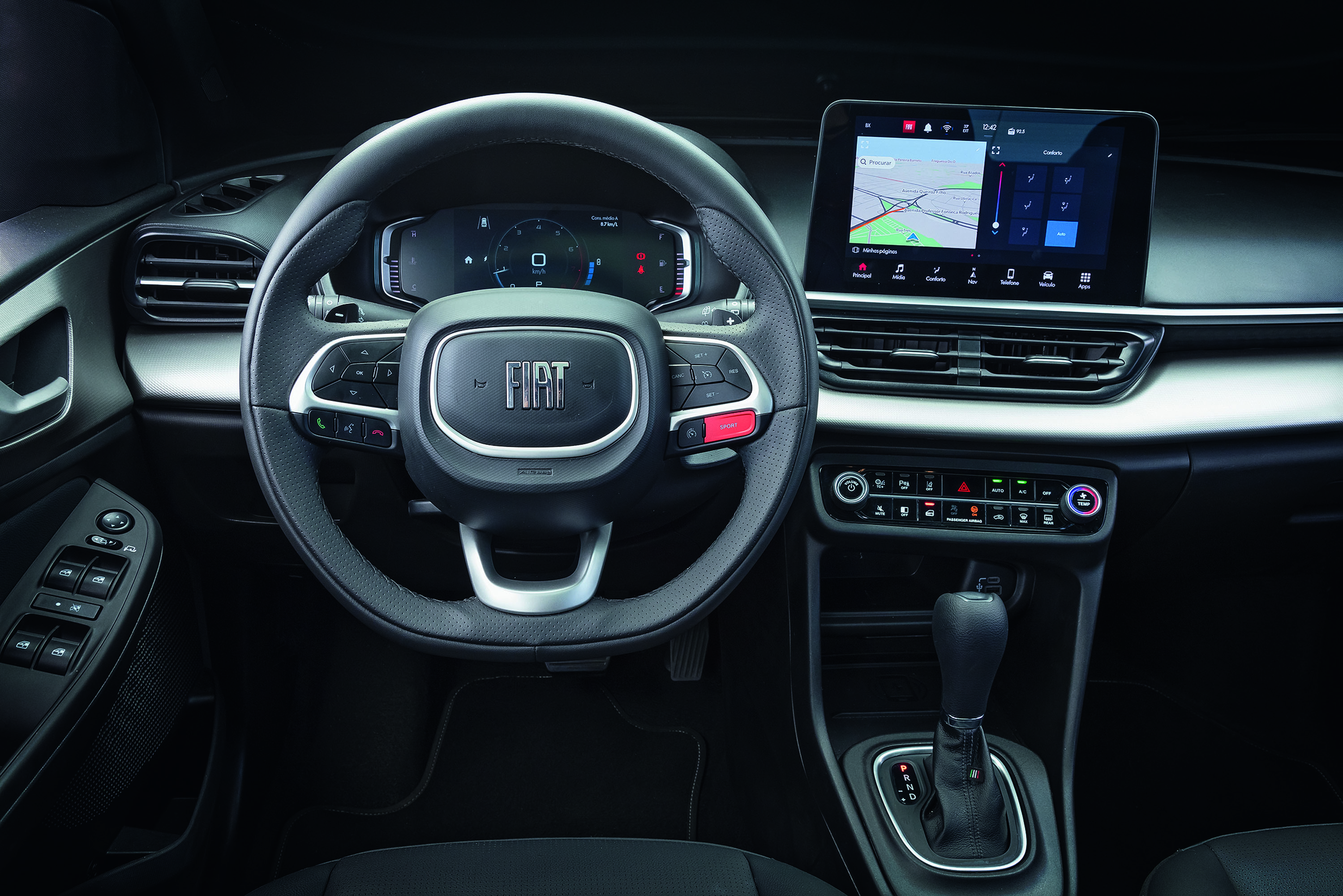 Interior de um carro Fiat com volante multifuncional, painel digital e tela multimídia exibindo um mapa de navegação. O câmbio automático e os controles do ar-condicionado estão visíveis no console central. O acabamento é em tons escuros e prata.