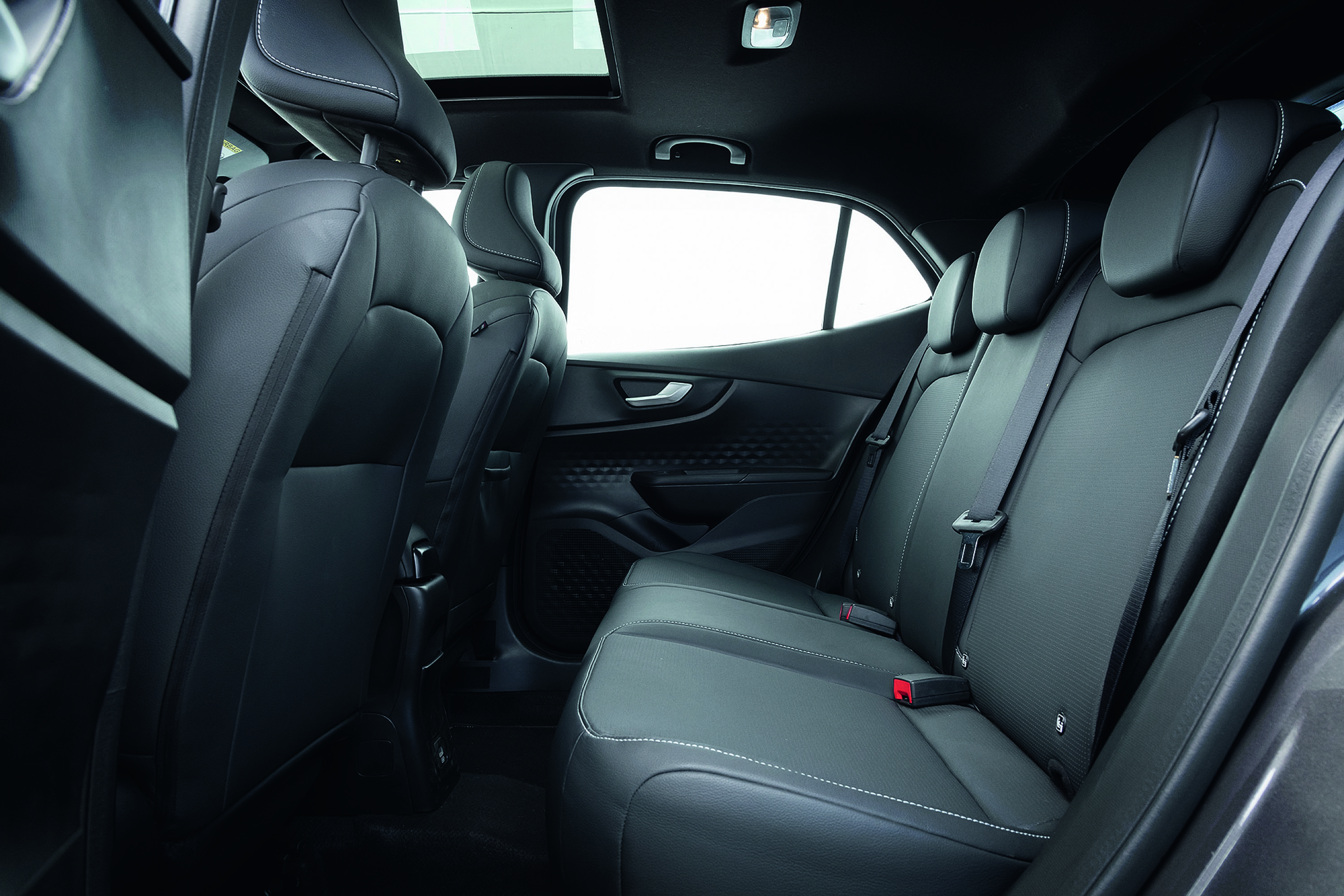 Interior de um carro com bancos traseiros de couro preto e costura branca, cintos de segurança visíveis, teto solar e luz de cortesia acesa