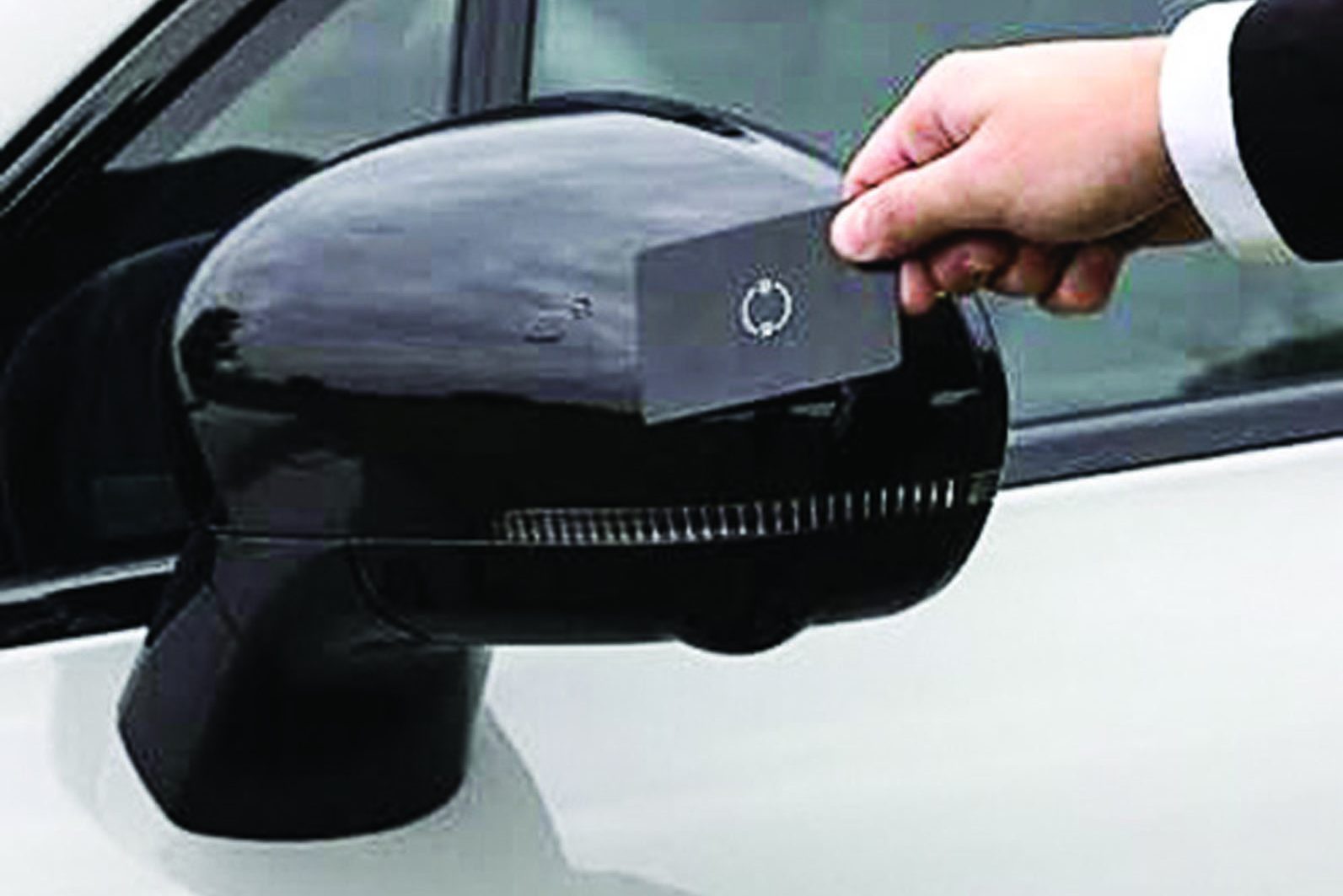 Mão masculina, vestindo terno escuro e camisa branca, encosta um cartão preto com um símbolo de recarregar em um retrovisor lateral preto de um carro branco
