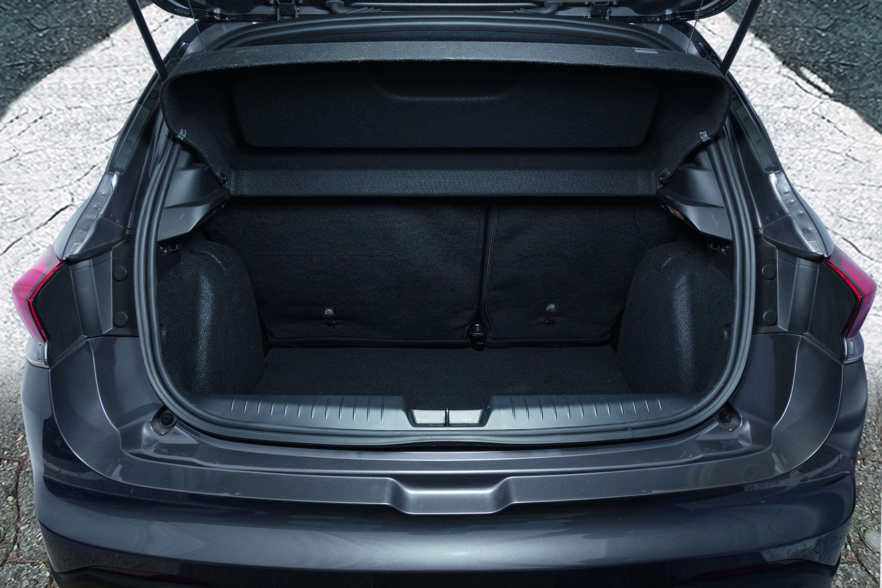Traseira de um carro hatchback cinza-escuro com o porta-malas aberto, mostrando o amplo espaço interno e o banco traseiro rebatido