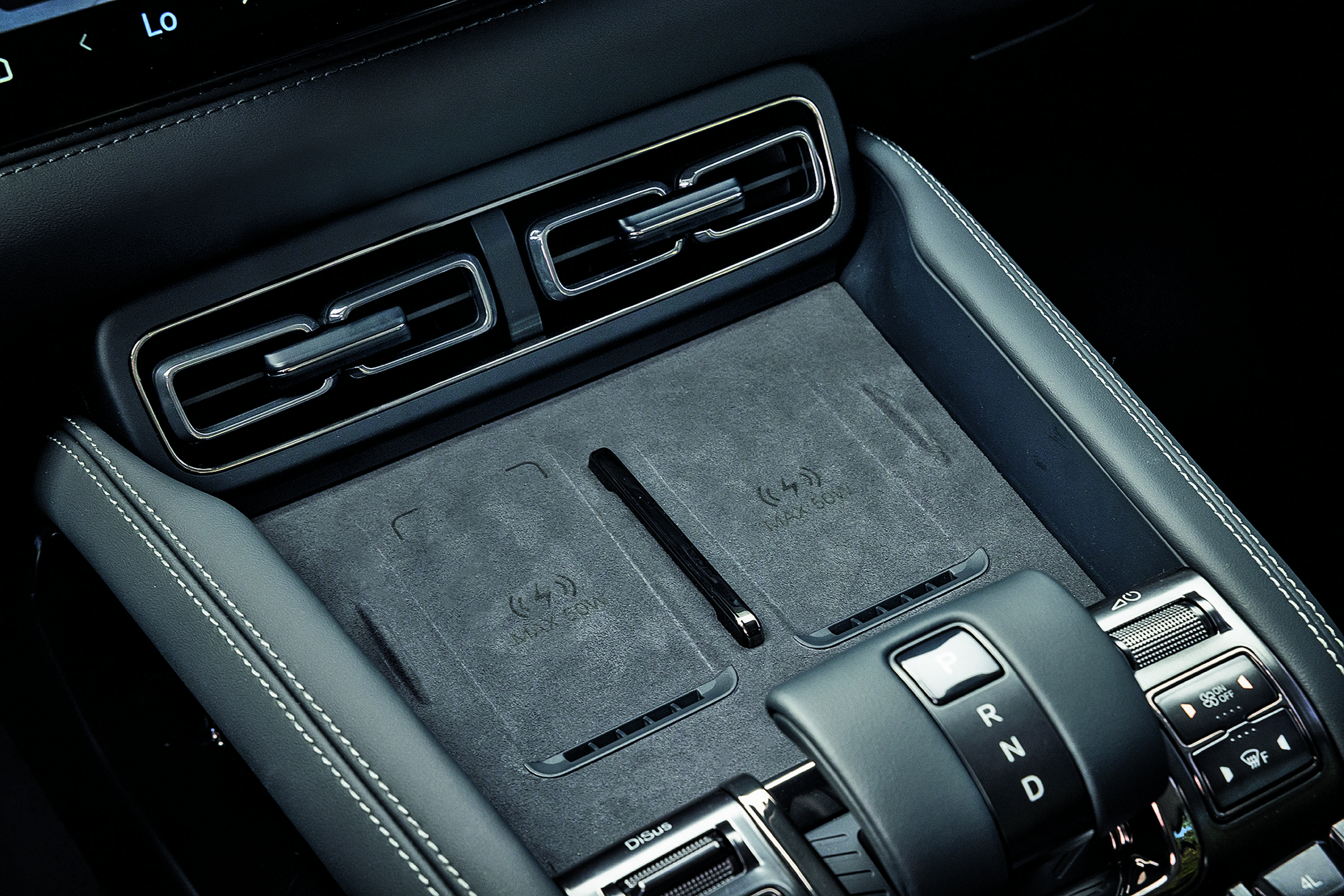 Interior de carro moderno com console central em couro preto e costura branca, dois carregadores de celular por indução, saídas de ar cromadas e alavanca de câmbio automática
