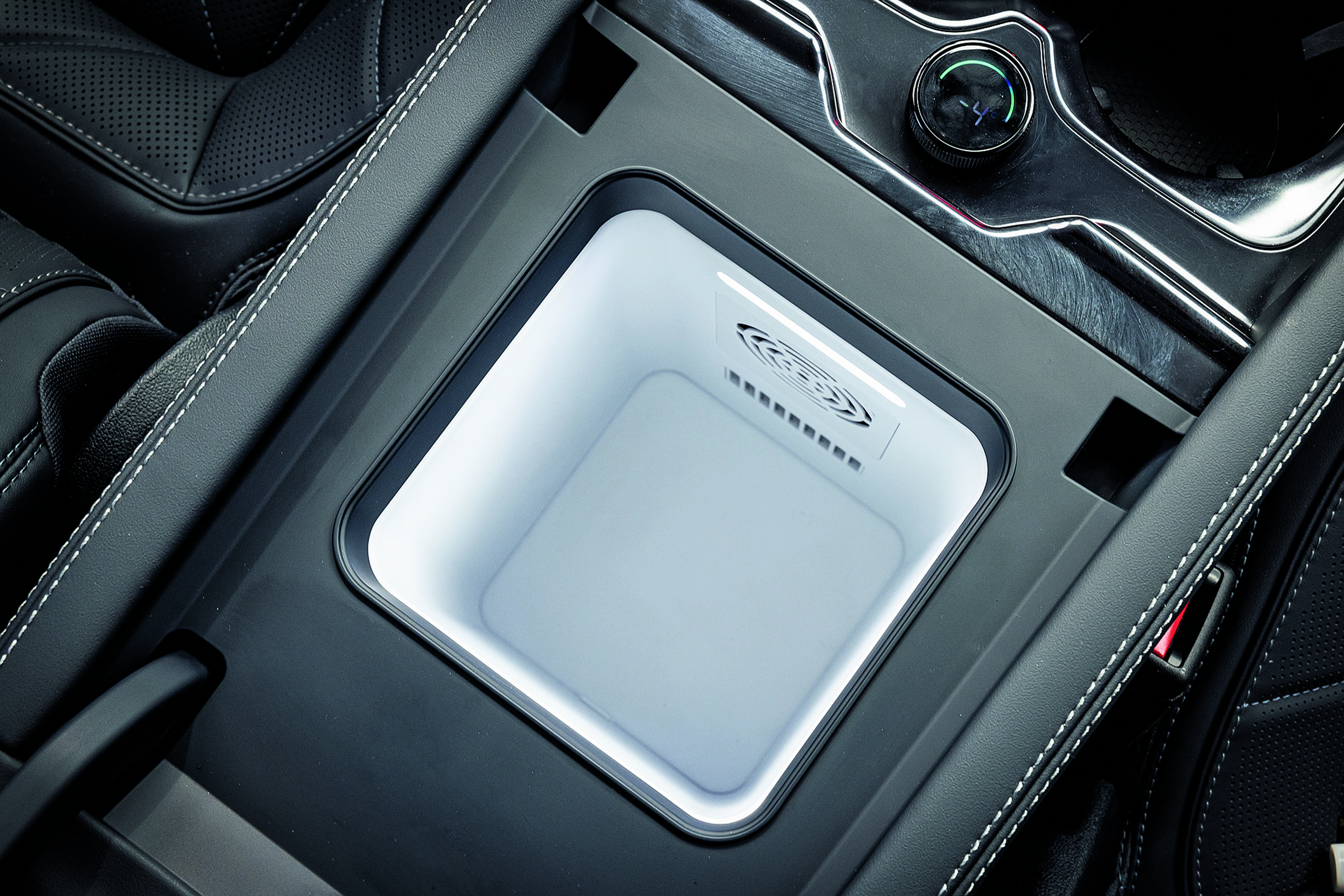 Compartimento refrigerado iluminado em branco no console central de um carro, com detalhes em couro preto e costura branca