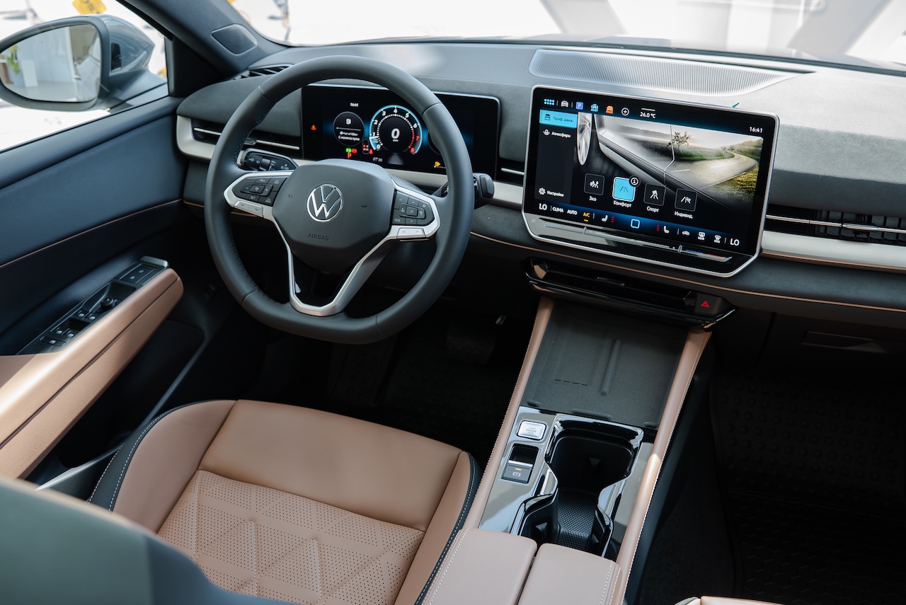 Interior de um carro moderno com volante multifuncional da Volkswagen, painel digital e uma grande tela multimídia exibindo um mapa de navegação. Os bancos são de couro bege perfurado, e o console central tem acabamento em preto brilhante e bege