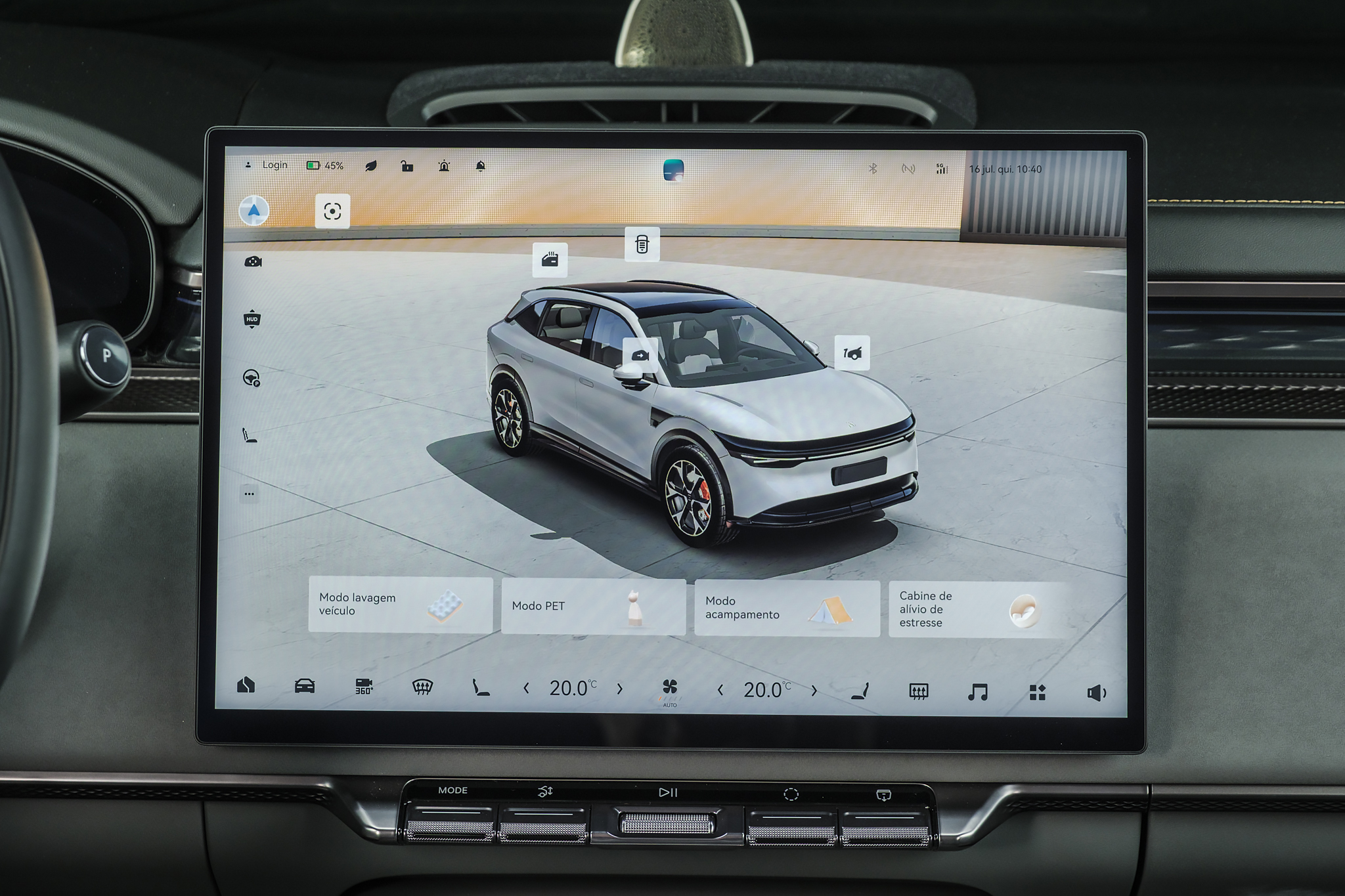 Tela multimídia de carro exibindo um SUV branco em 3D com opções de controle do veículo, como Modo lavagem veículo, Modo PET, Modo acampamento e Cabine de alívio de estresse. A tela mostra também ícones de configurações, temperatura e mídia, com o volante do carro visível à esquerda